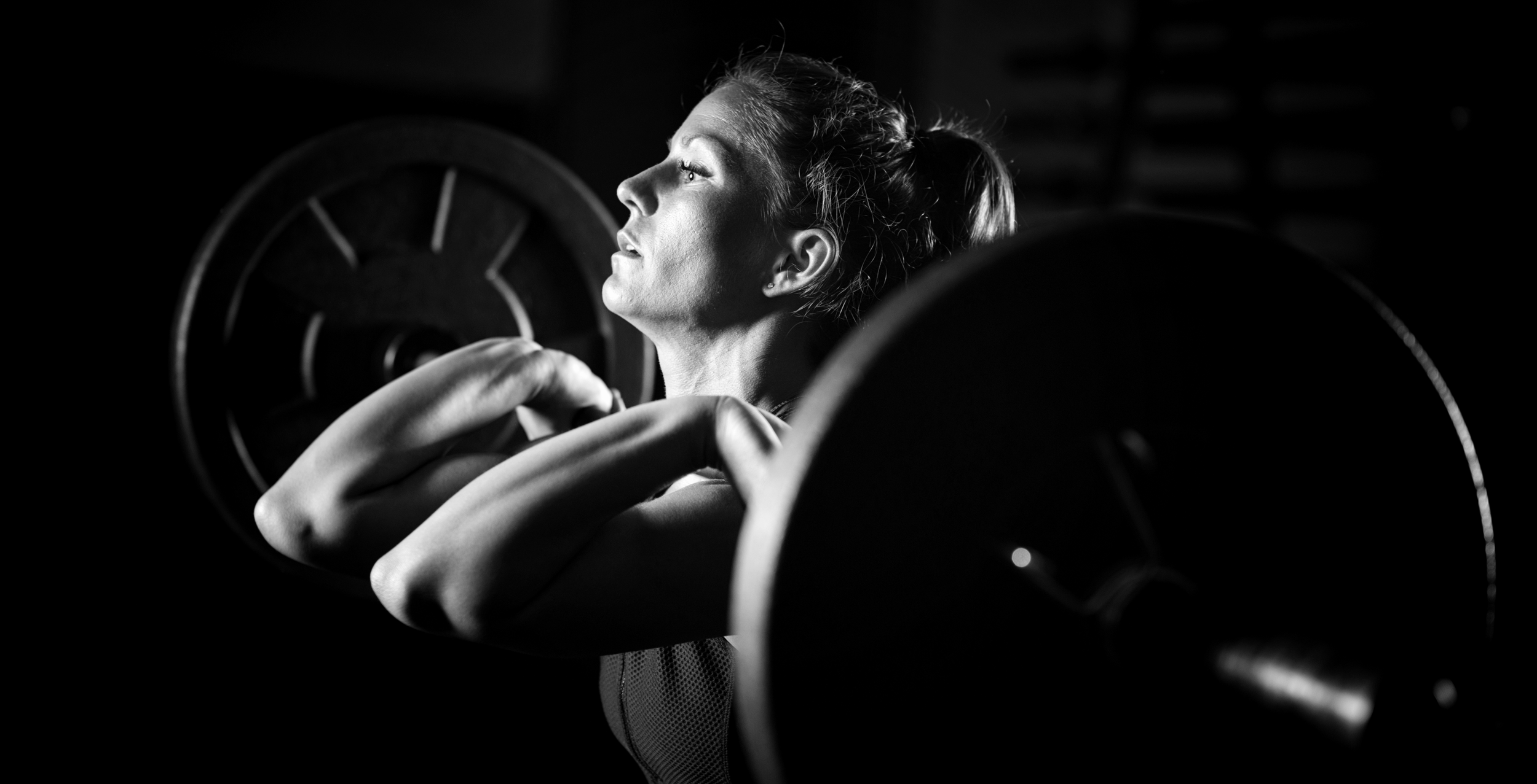 Black and white photo of a woman lifting barbells in a gym, focused expression.