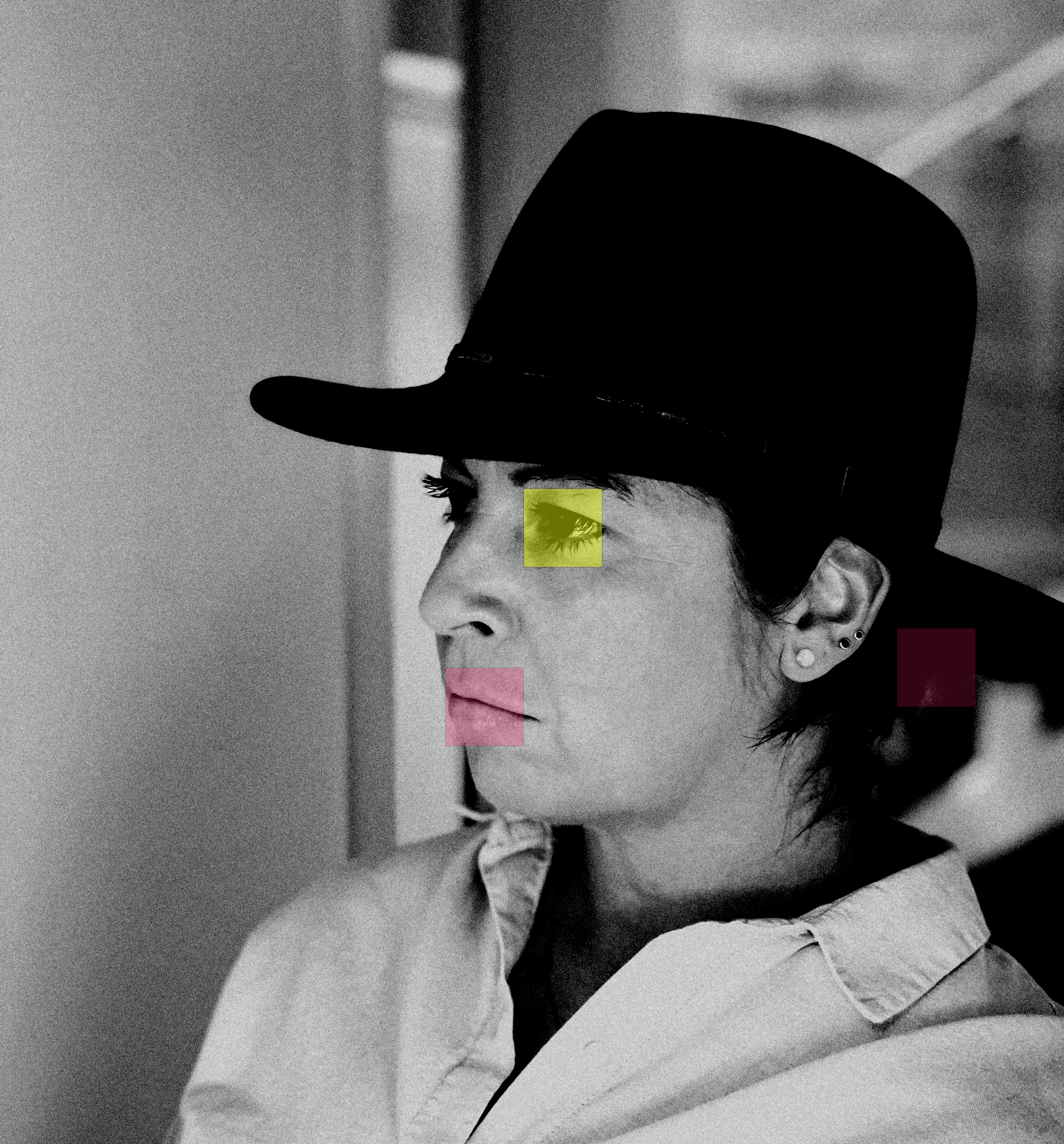 Black and white photograph of a woman with dark eye makeup and earrings, wearing a wide-brimmed hat, with her face partially visible.