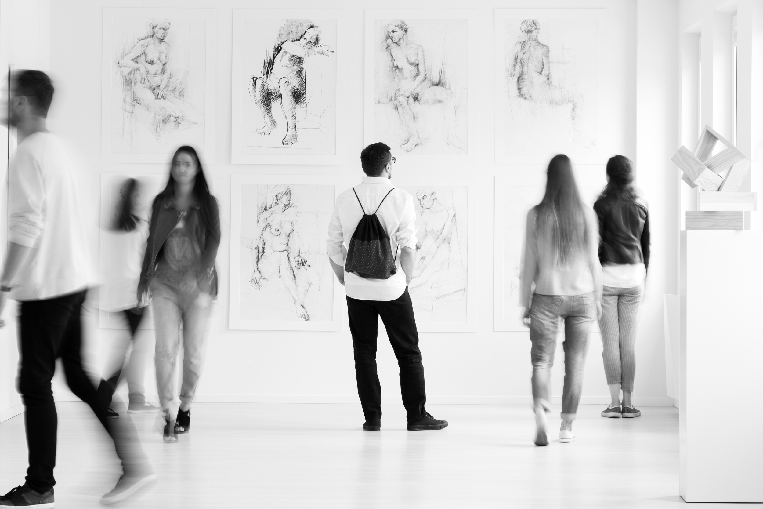 People walking around an art gallery with sketches of nude figures on the wall.