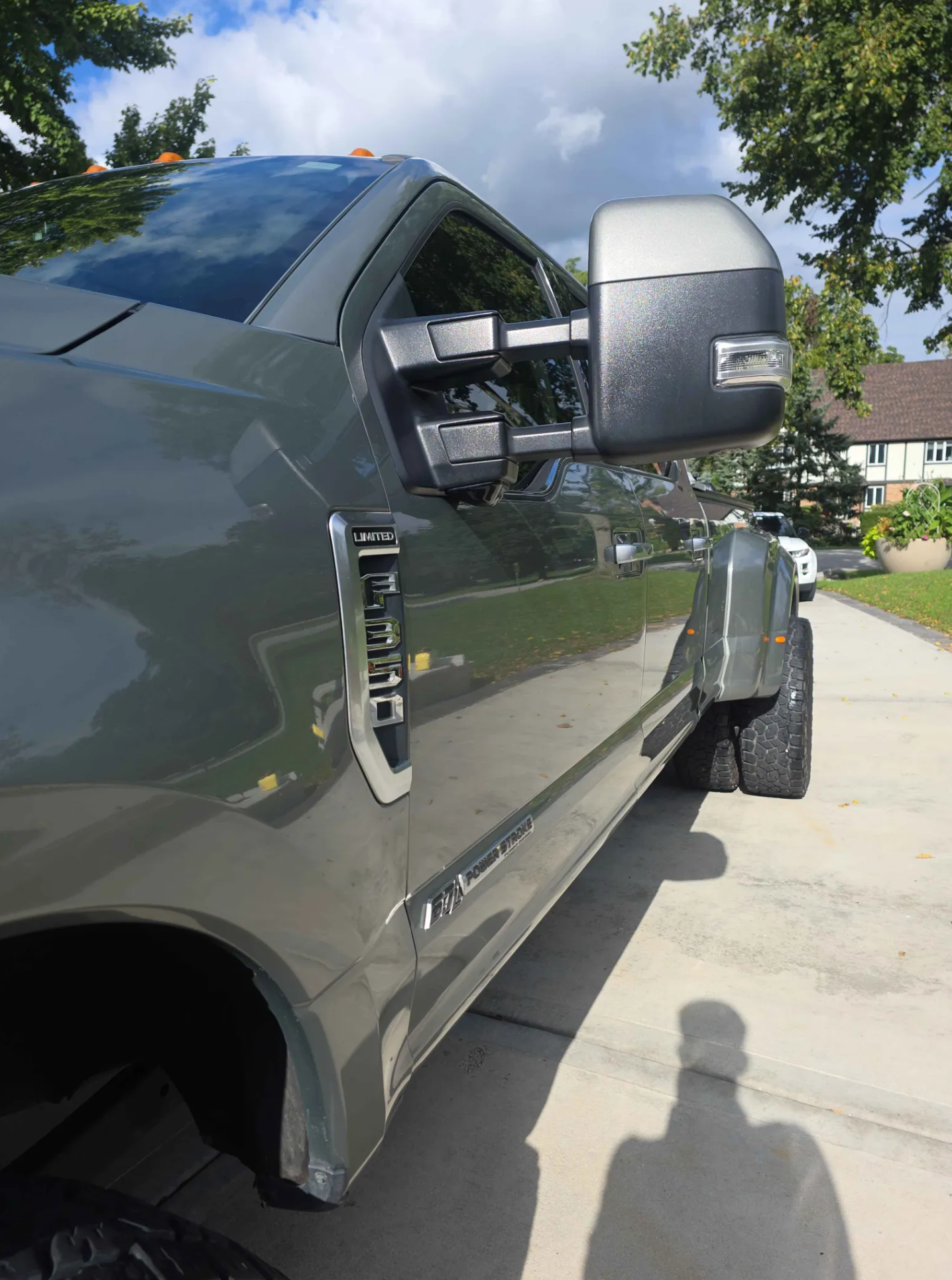 A gray pickup truck parked on a driveway with trees and a house in the background, under a partly cloudy sky.