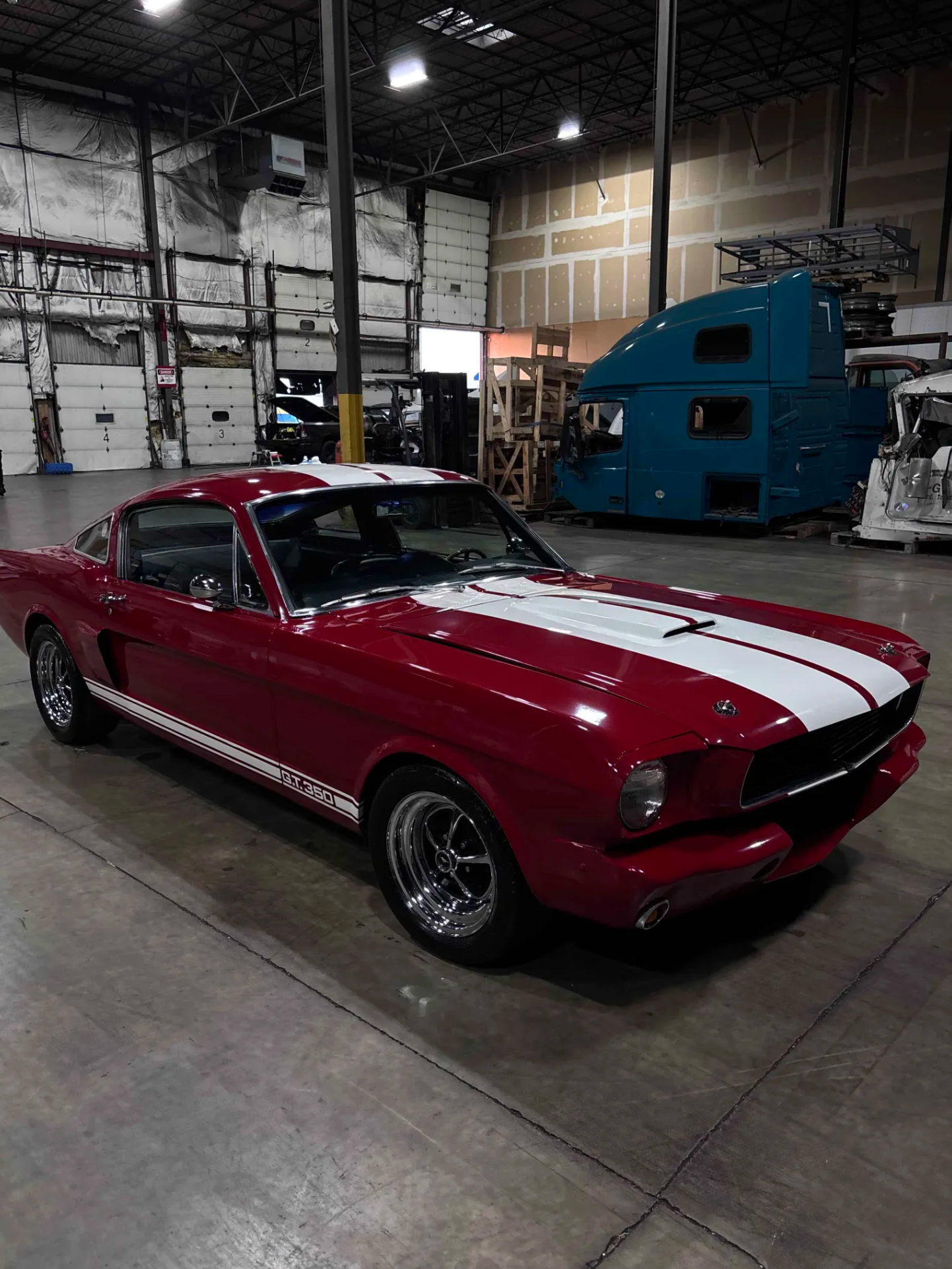 A red vintage Chevrolet Corvette sports car with white racing stripes parked inside a warehouse.