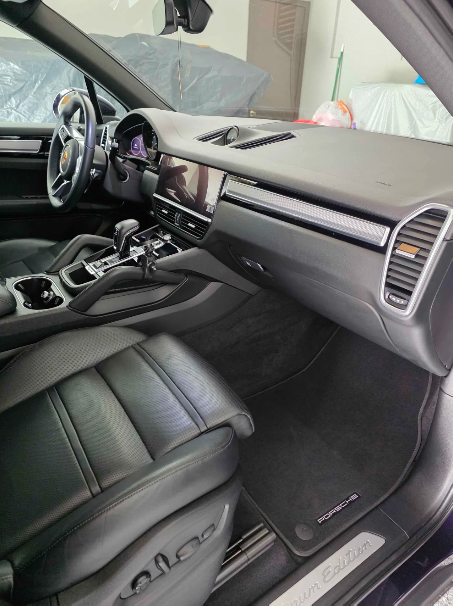 The interior of a luxury Porsche vehicle with black leather seats, digital dashboard, and modern dashboard controls. The car showcases premium design, with a view of the driver and passenger area, including the center console, gear shifter, and steer