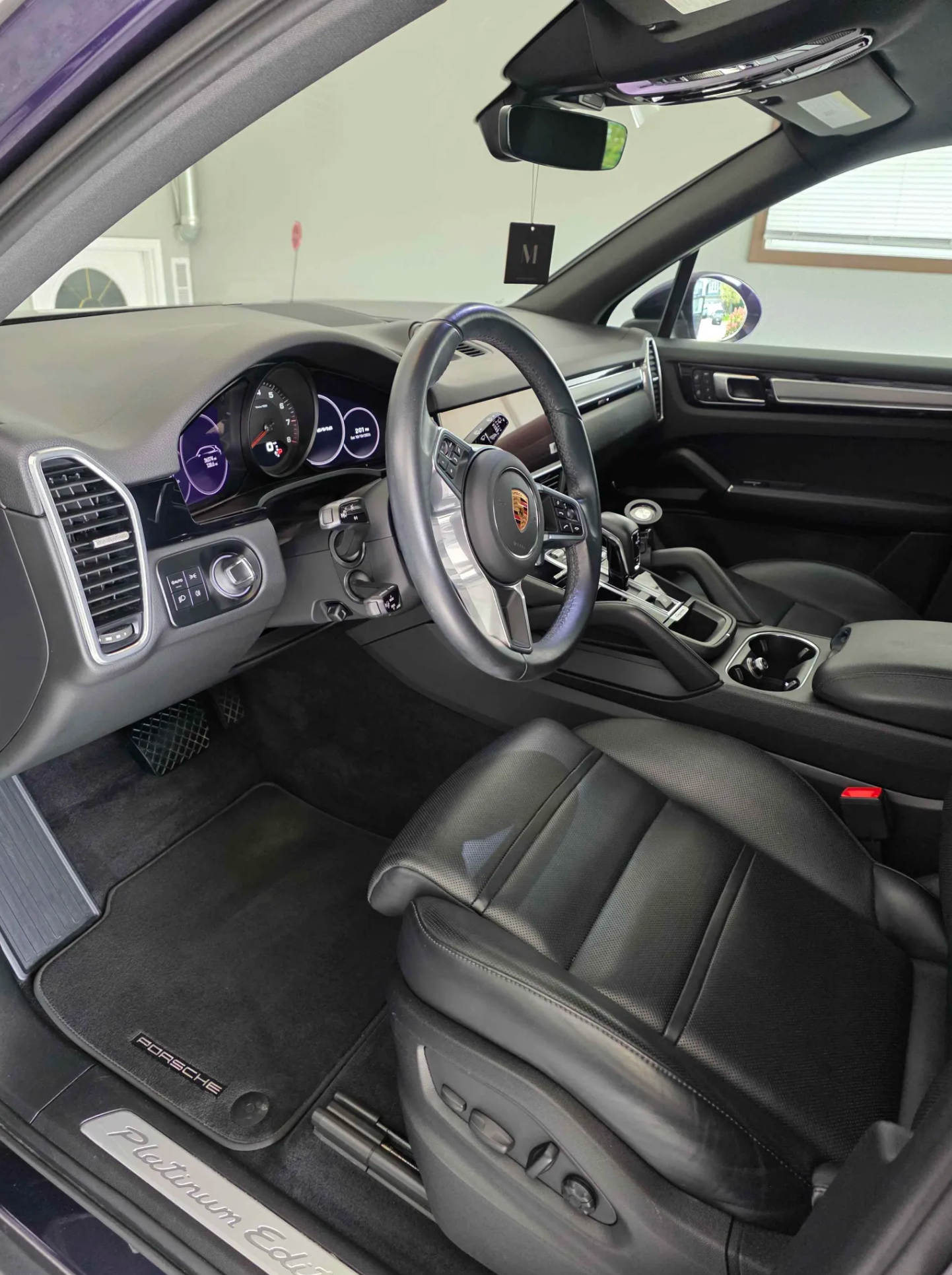 Interior of a black Porsche vehicle with leather seats, digital dashboard, and gear shift, parked indoors near a window.