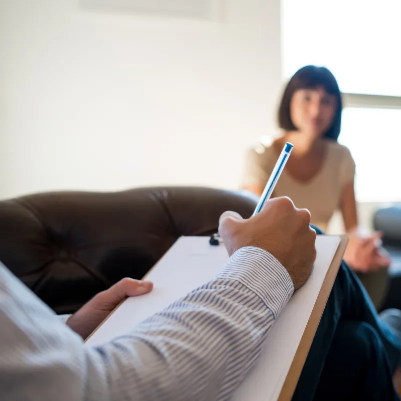 A psychotherapist is taking notes on a writing pad in front of a patient.