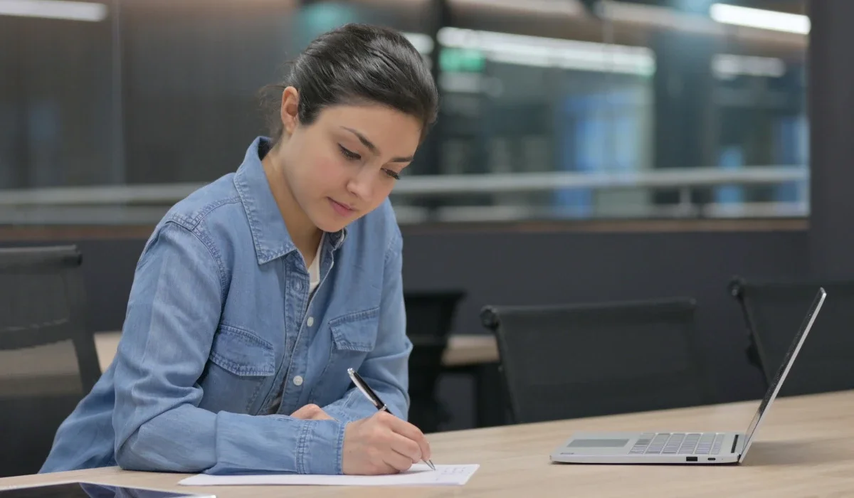 Woman writing in a notebook at a desk, practicing journaling to manage rumination