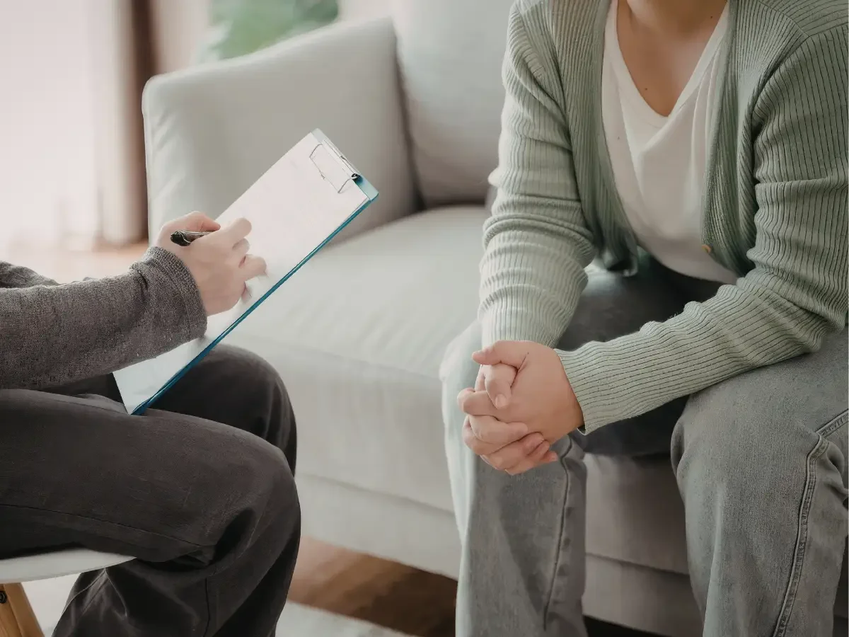 Therapist holding a notepad, seated across from a person on a couch during a counselling session