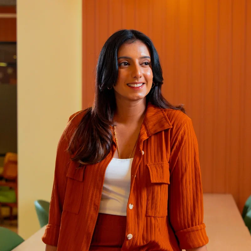 A woman wearing an orange outfit is smiling inside a modern office.
