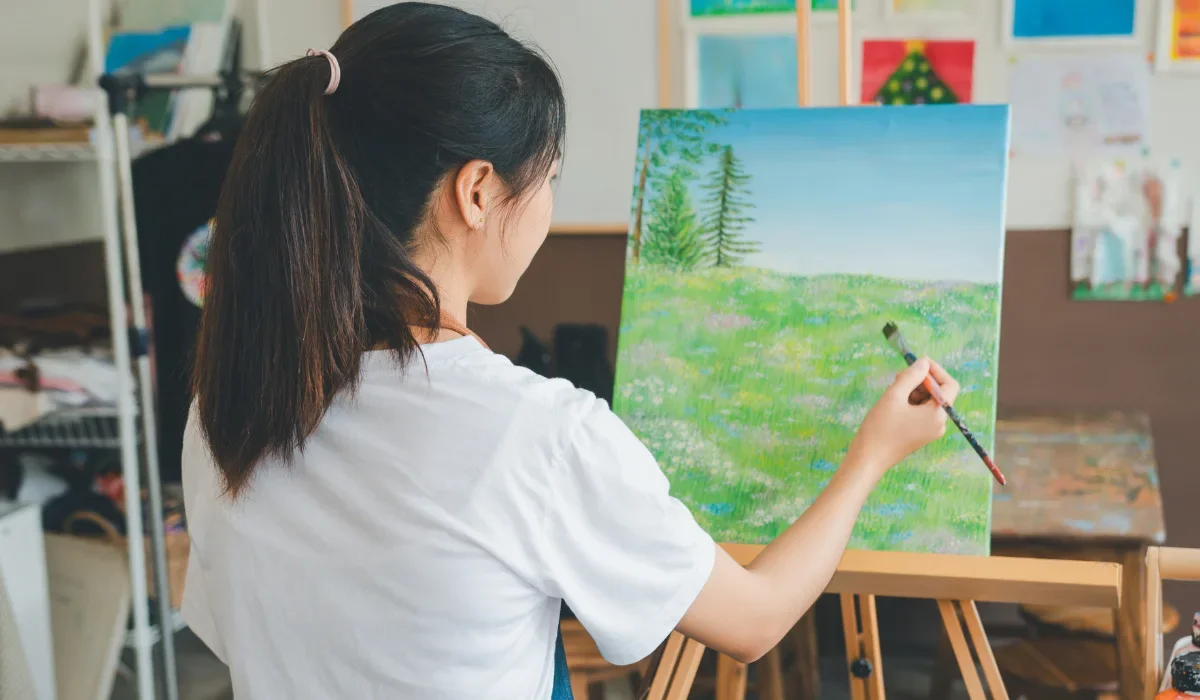 A person is painting a landscape on a canvas in an art studio.