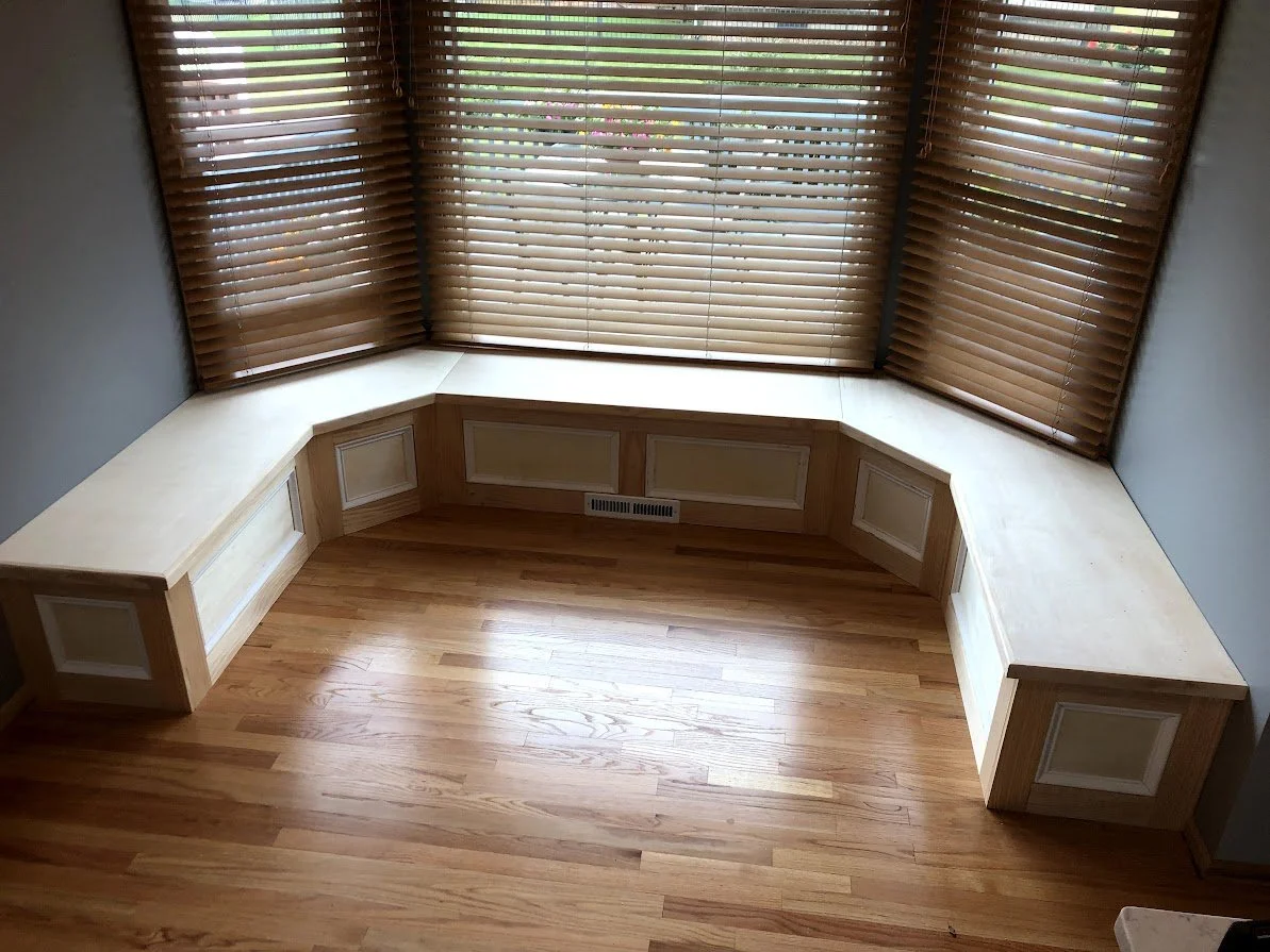 Empty corner window seat with wooden paneling and blinds in a room with hardwood flooring.