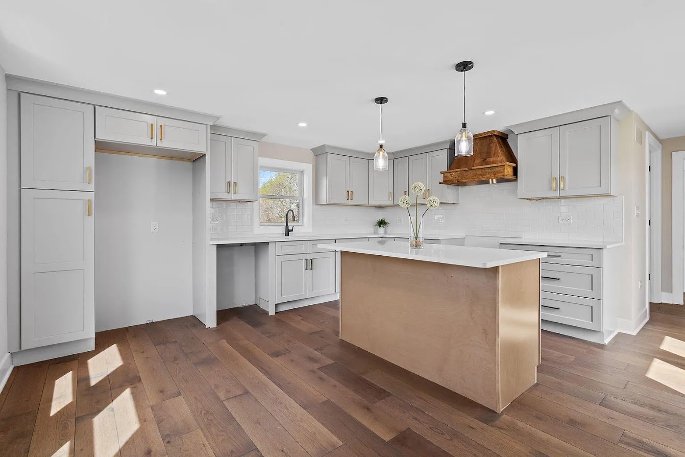 Modern kitchen with white cabinets, a wooden island, pendant lights, hardwood floors, and a small window above the sink.