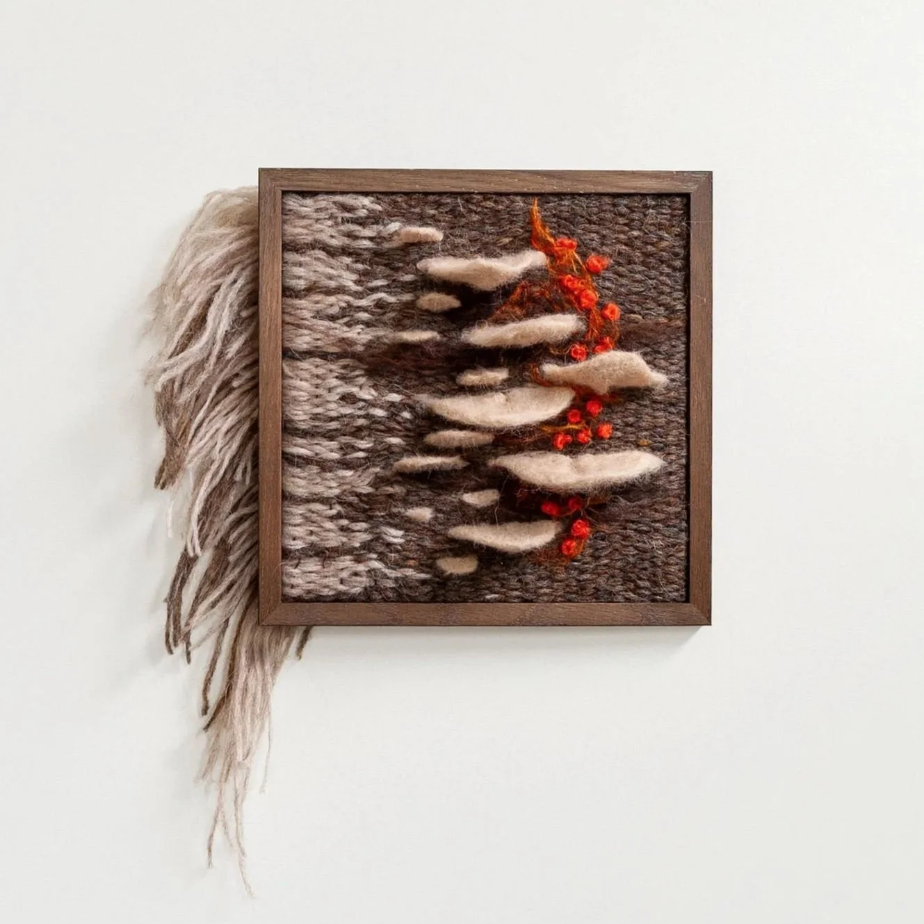 cream colored felt mushrooms on brown and cream woven tapestry framed in walnut frame with fire red accents