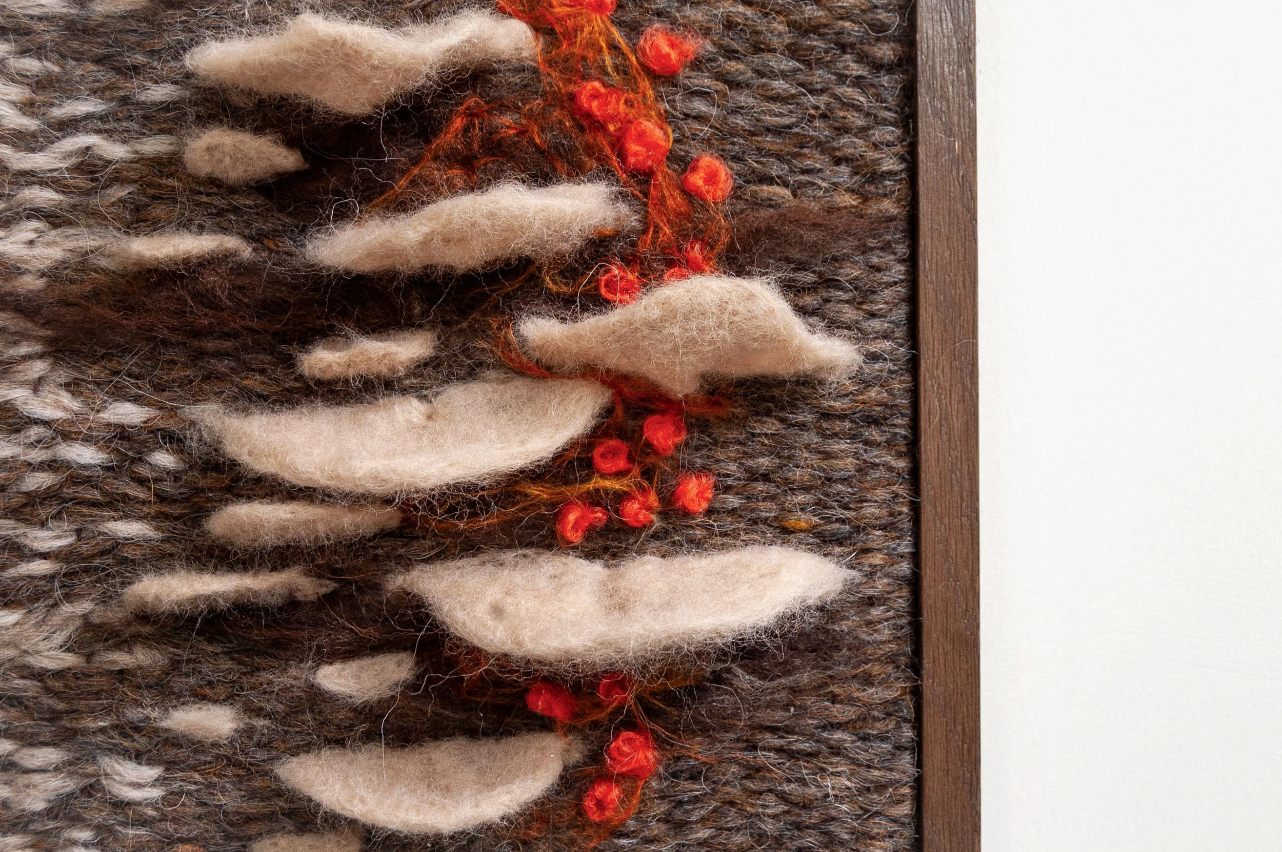 cream colored felt mushrooms on brown and cream woven tapestry framed in walnut frame with fire red accents