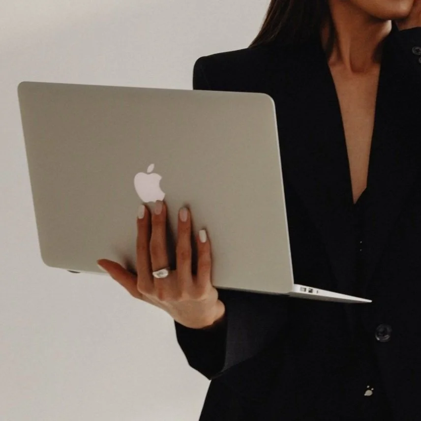 Person in a black blazer holding a silver MacBook laptop.
