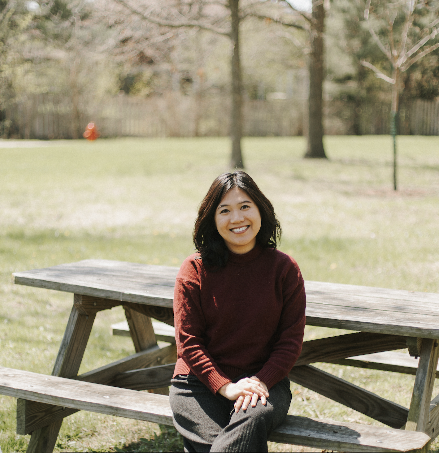 Tsuki LMFT smiling, seated at a picnic table in a park with her hands in her lap