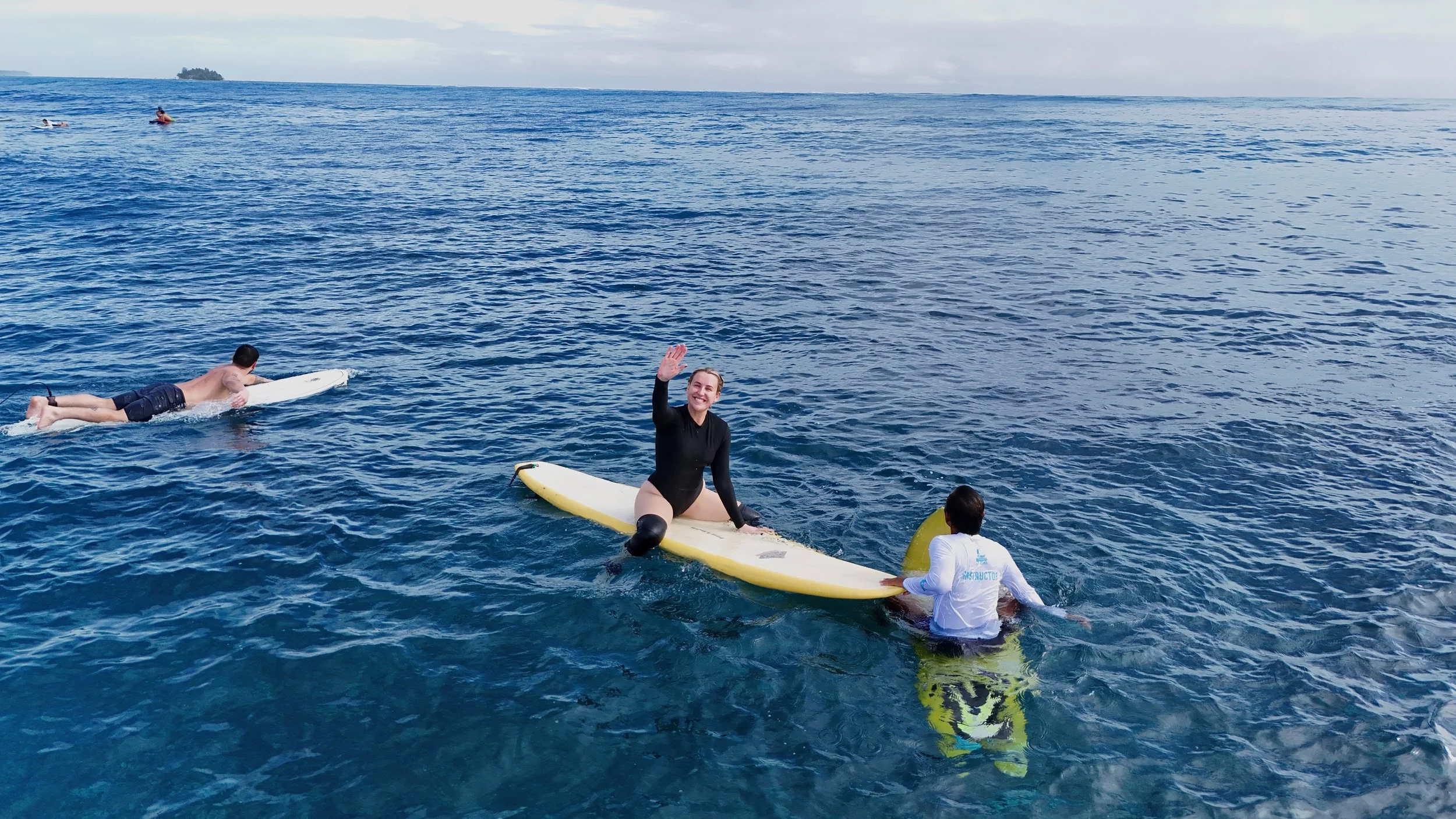 2 men walking out in the shallows to go surfing carrying their surfboards and are surrounded by dogs
