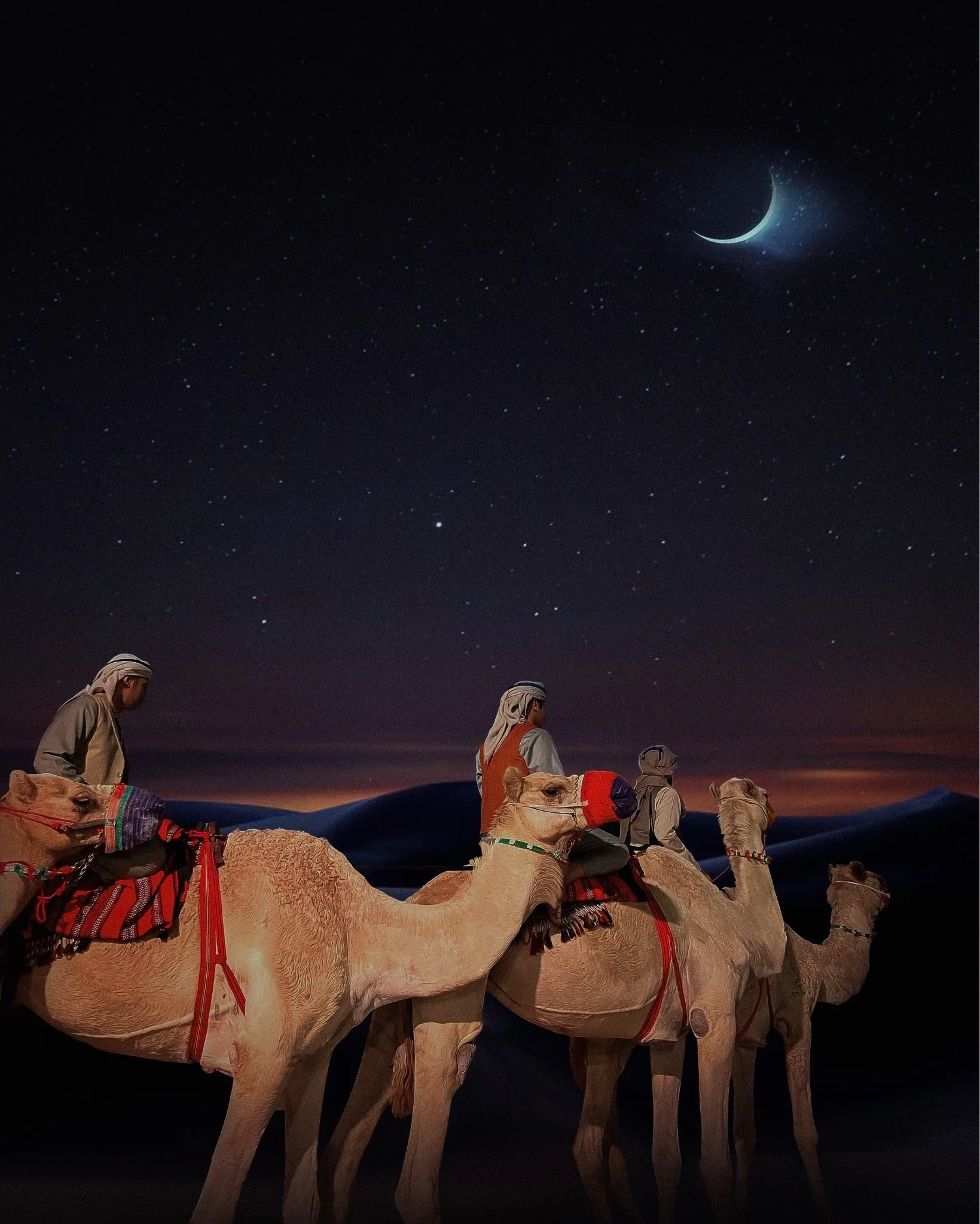 Four people wearing traditional desert clothing riding camels across sand dunes at night under a starry sky with a crescent moon.