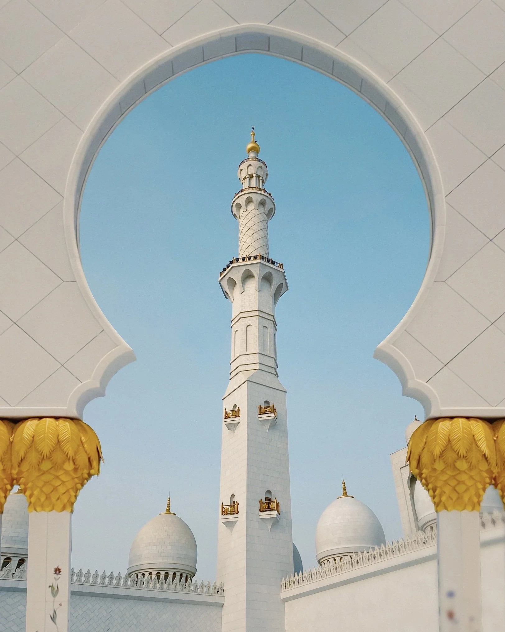 View of the minaret of the Sheikh Zayed Grand Mosque through an ornate archway.