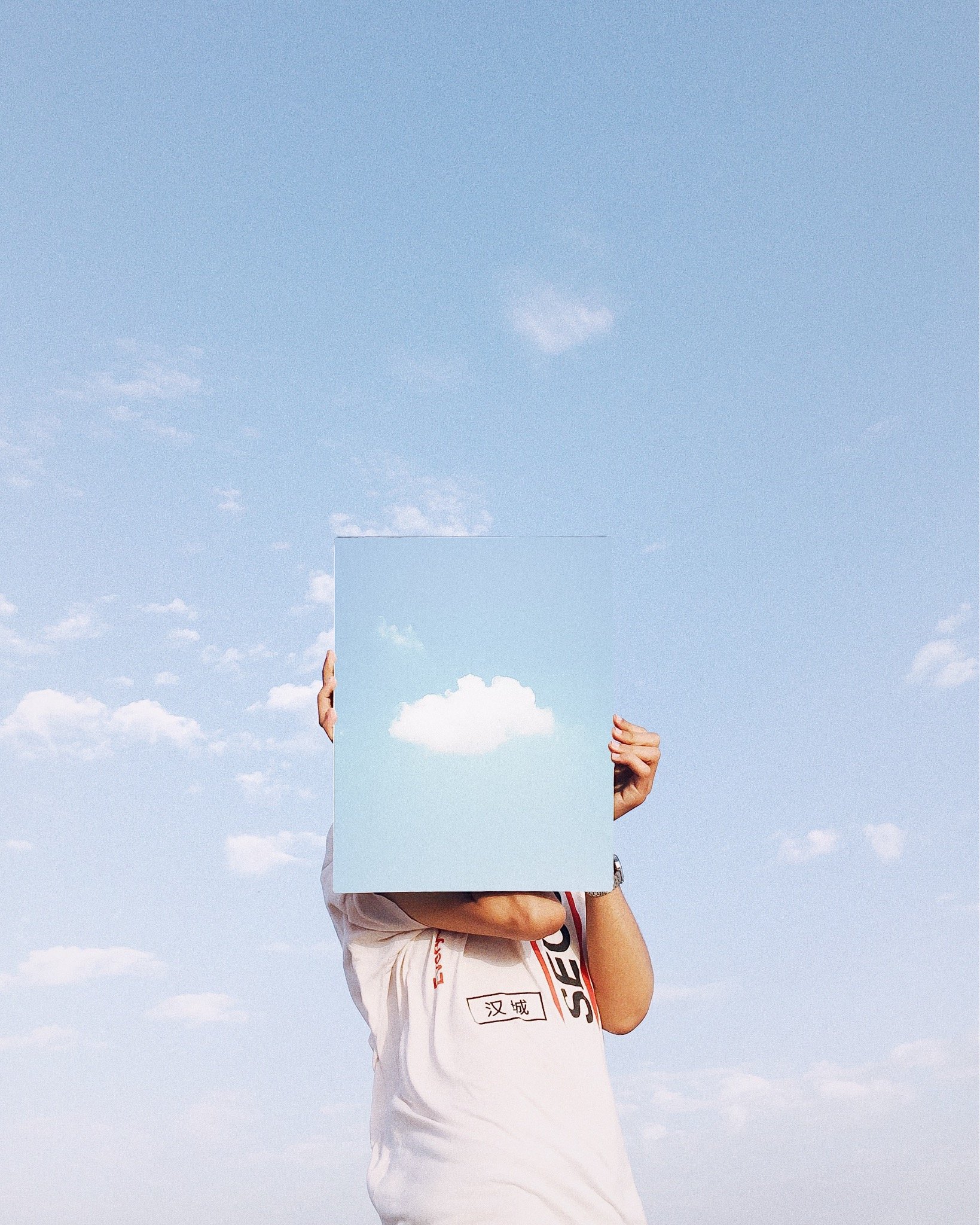 Person holding a mirror reflecting a cloud in the sky.