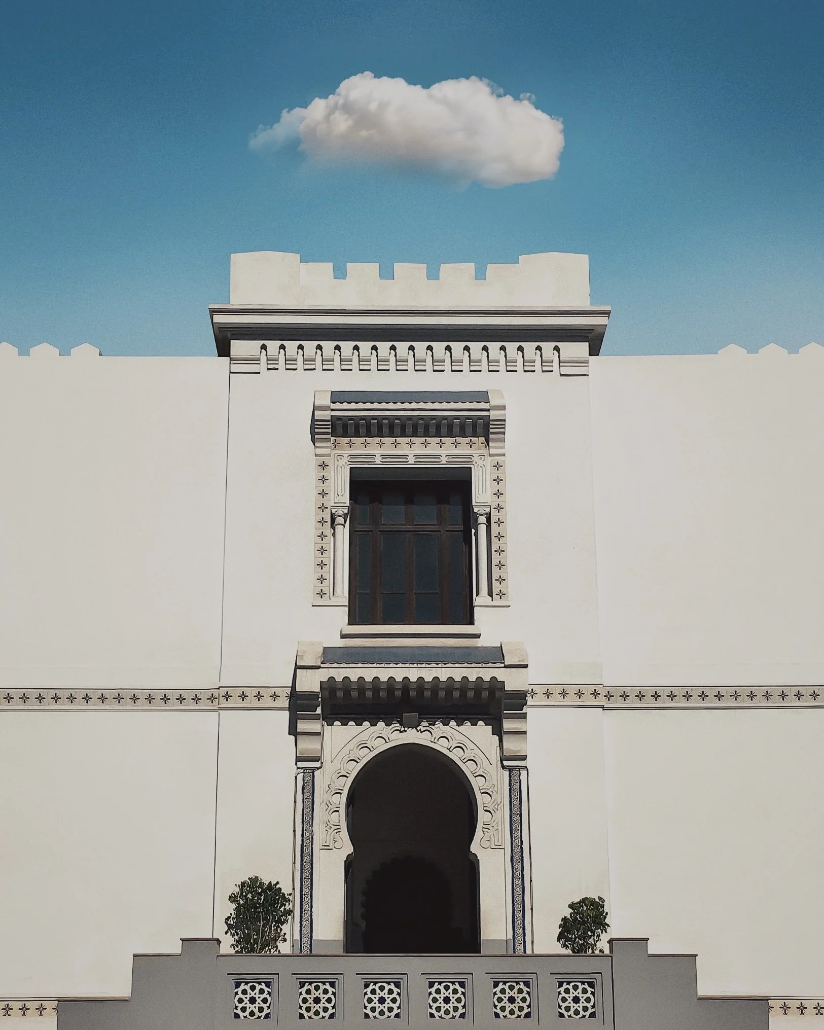 White building with decorative archway and ornate window, set against a blue sky with a single white cloud.