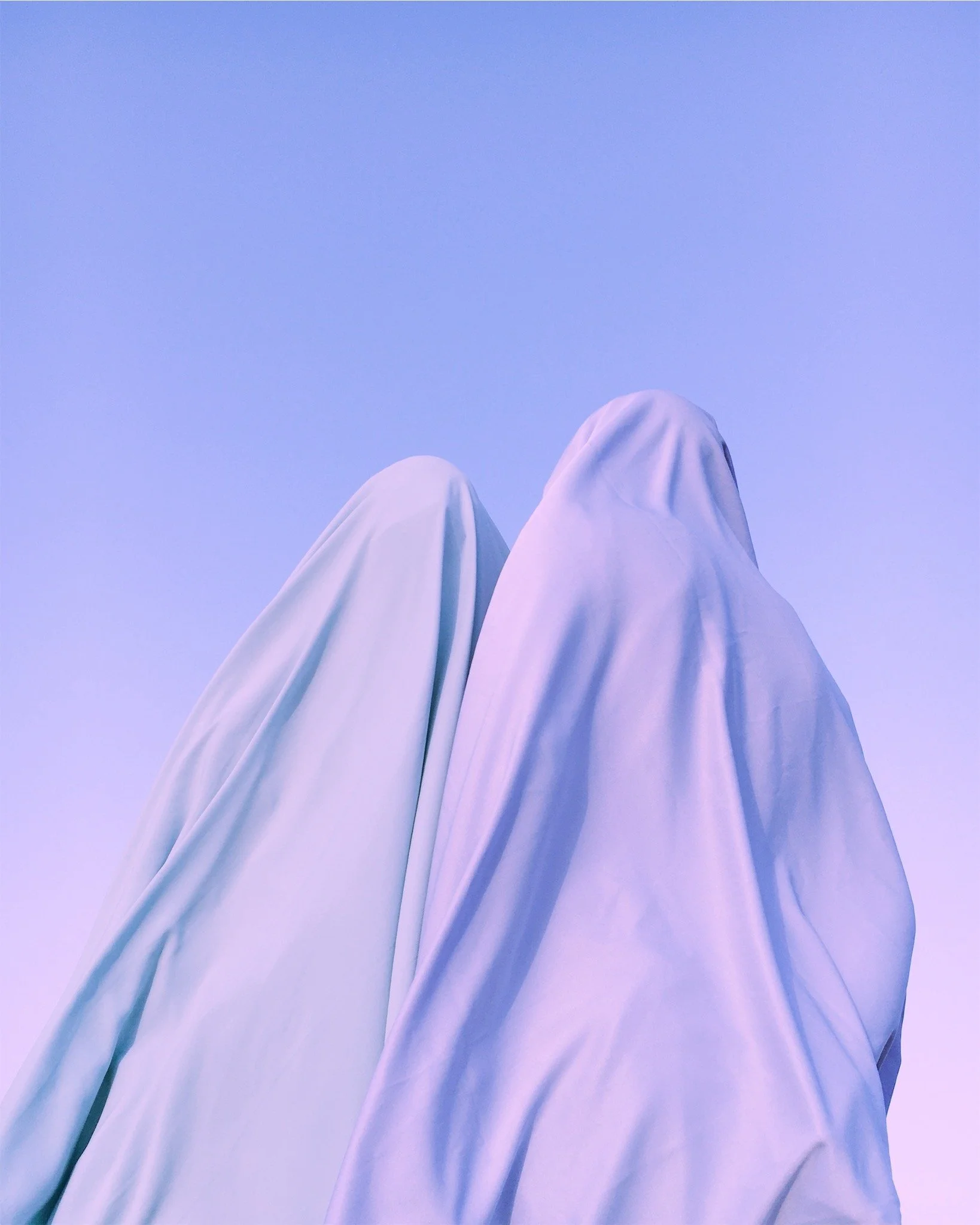 Two figures in white robes or shrouds sitting against a clear blue sky.
