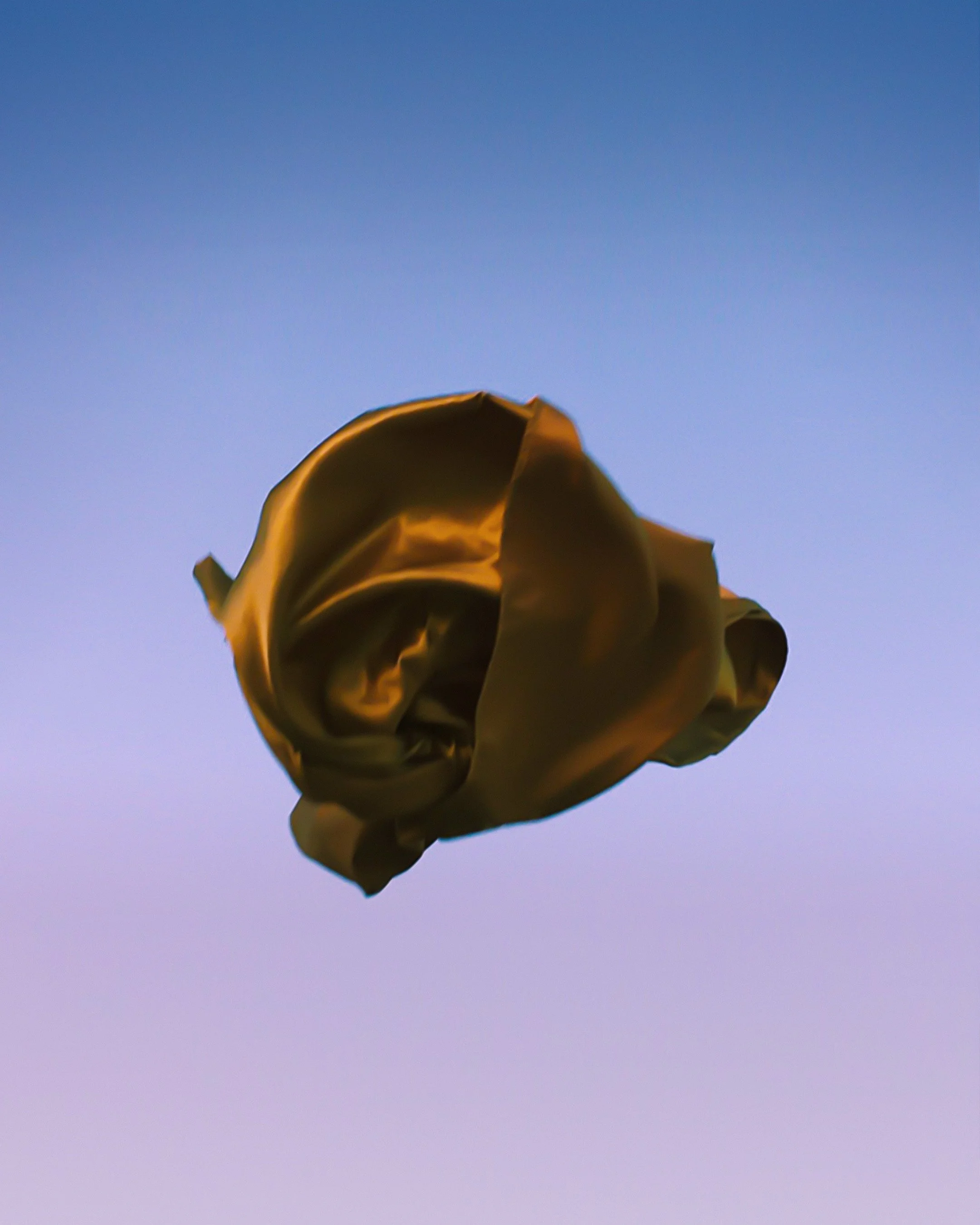 A gold-colored balloon shaped like a rose floating against a blue sky.