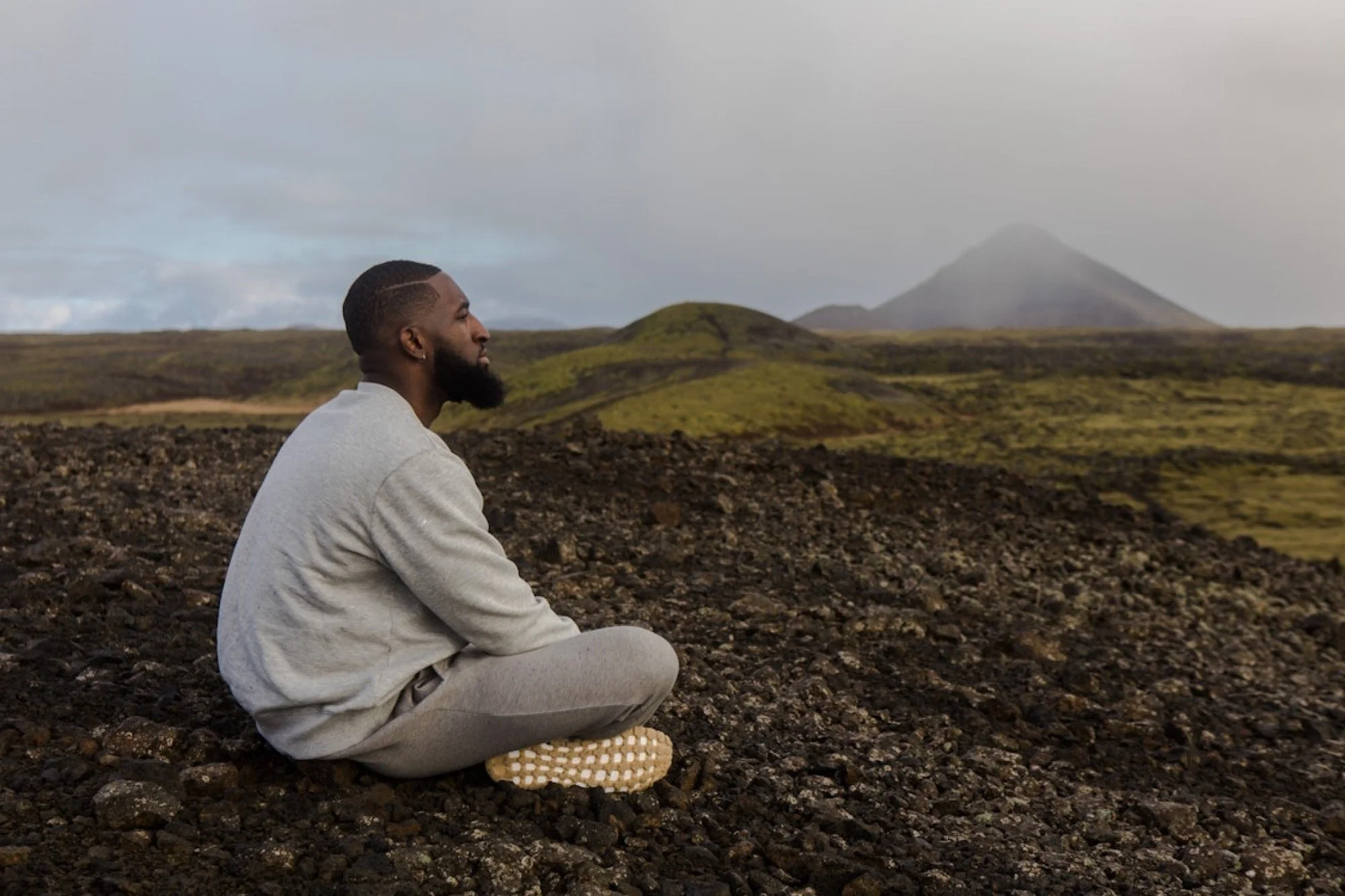 Man sat cross-legged with his eyes closed, facing a rugged landscape