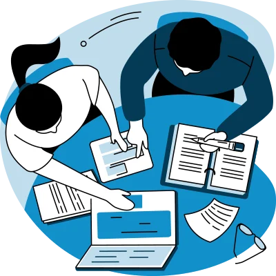 Two people working at a round table with laptops, tablets, documents, and a pen.