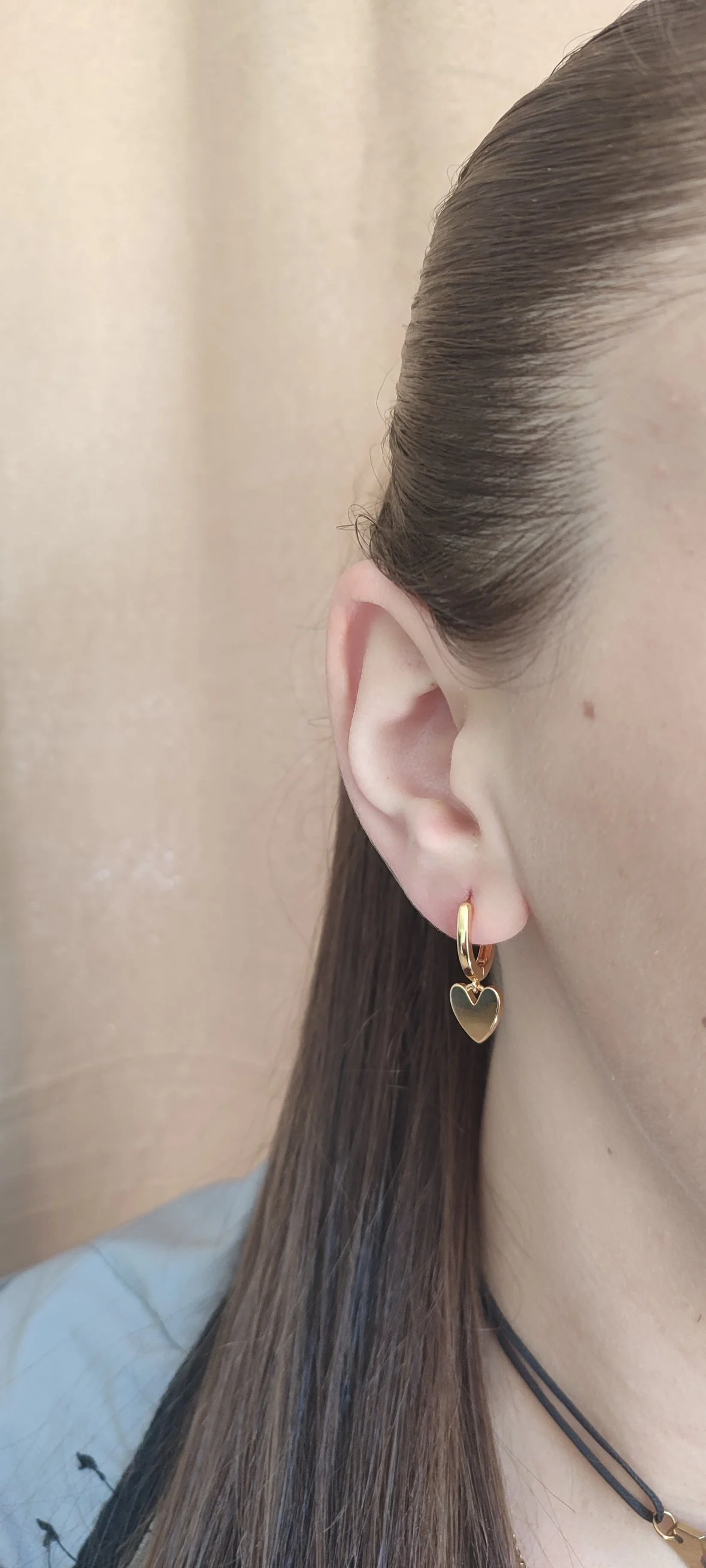 Une oreille avec une boucle d'oreille dorée en forme de cœur et des cheveux bruns lisses.