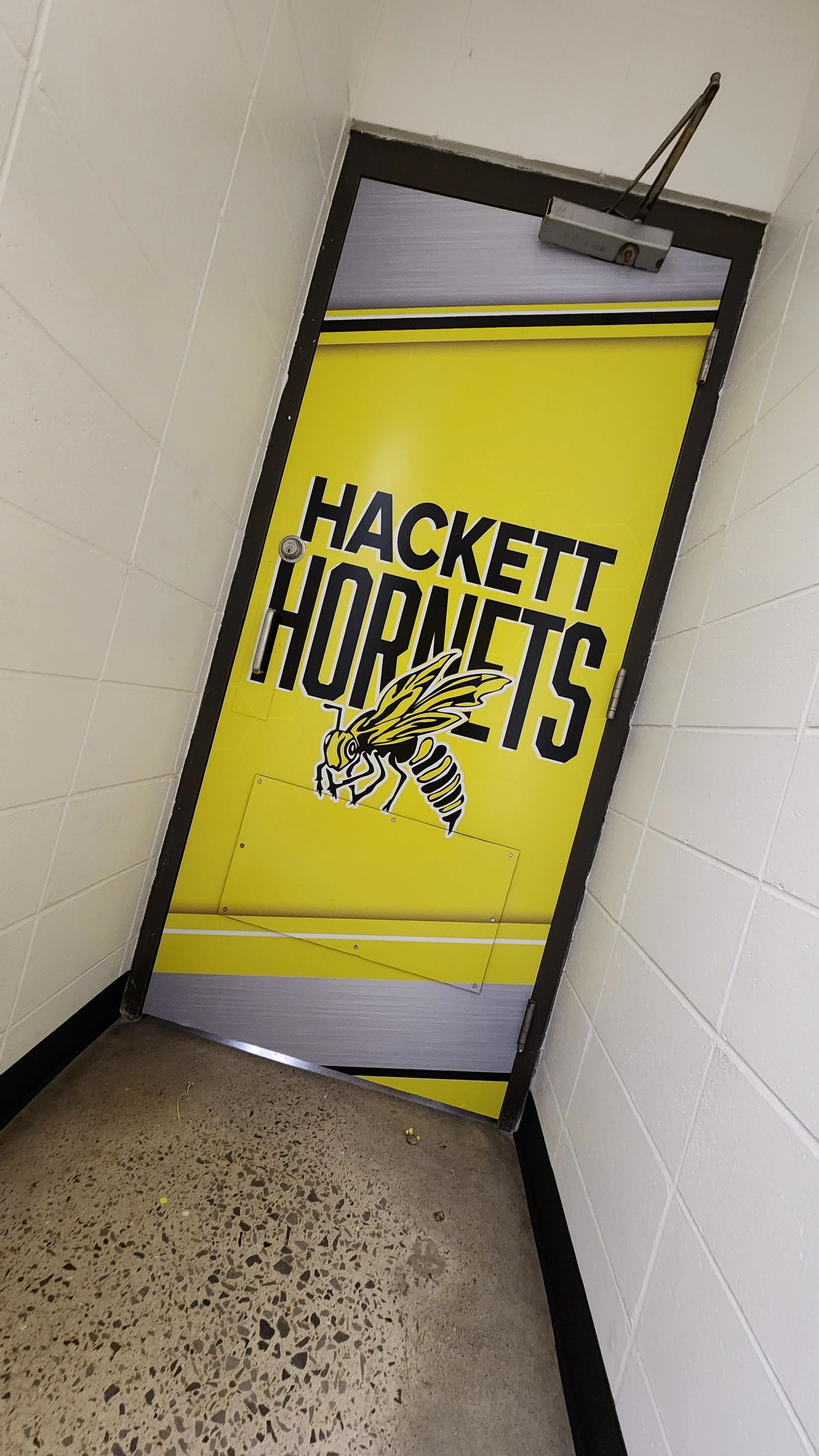 Yellow door featuring "Hackett Hornets" text and a hornet graphic, in a tiled hallway.