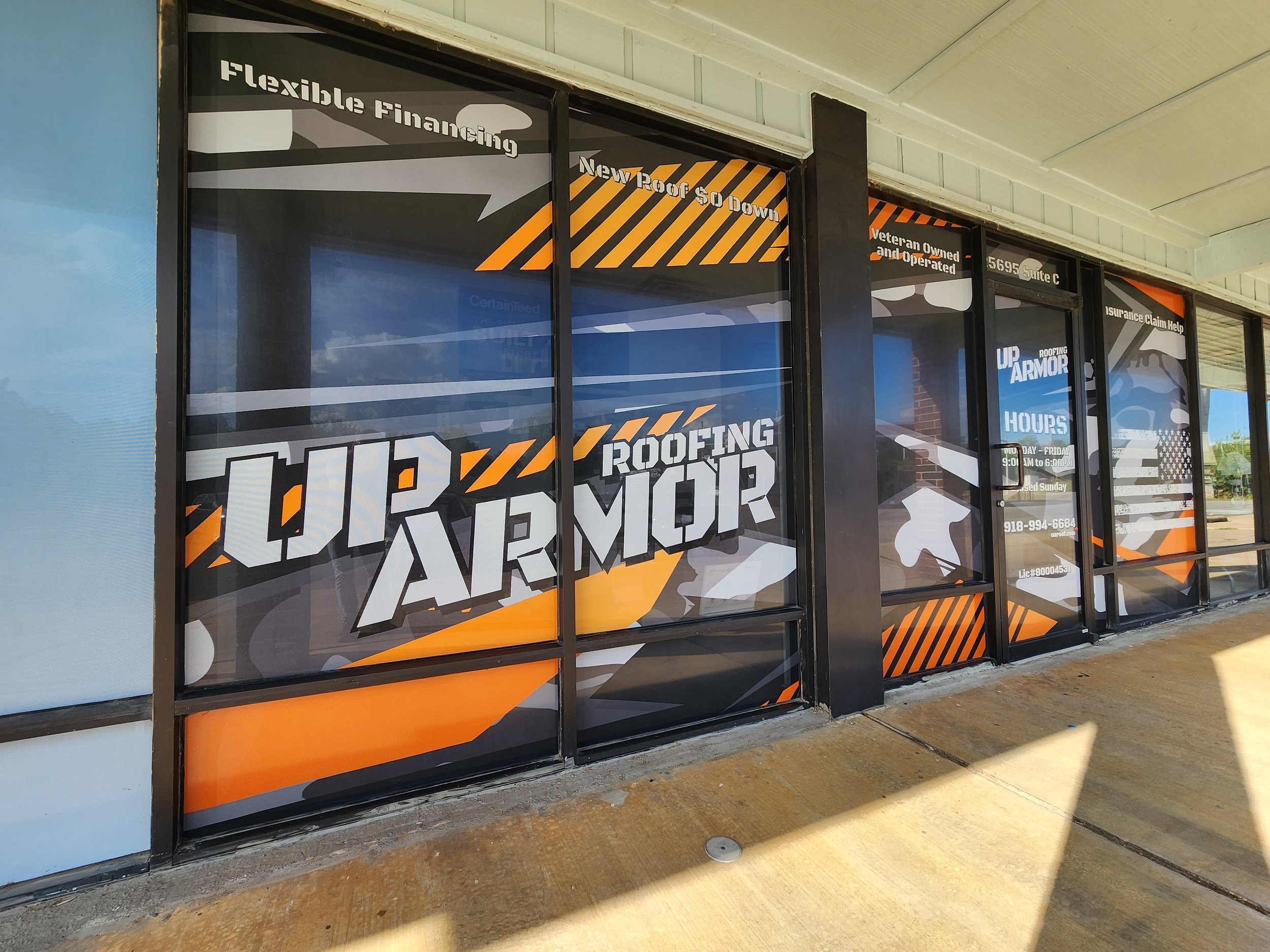 Storefront with window graphics for "Up Armor Roofing," featuring information about flexible financing, veteran ownership, services, and contact details in bold colors and patterns.