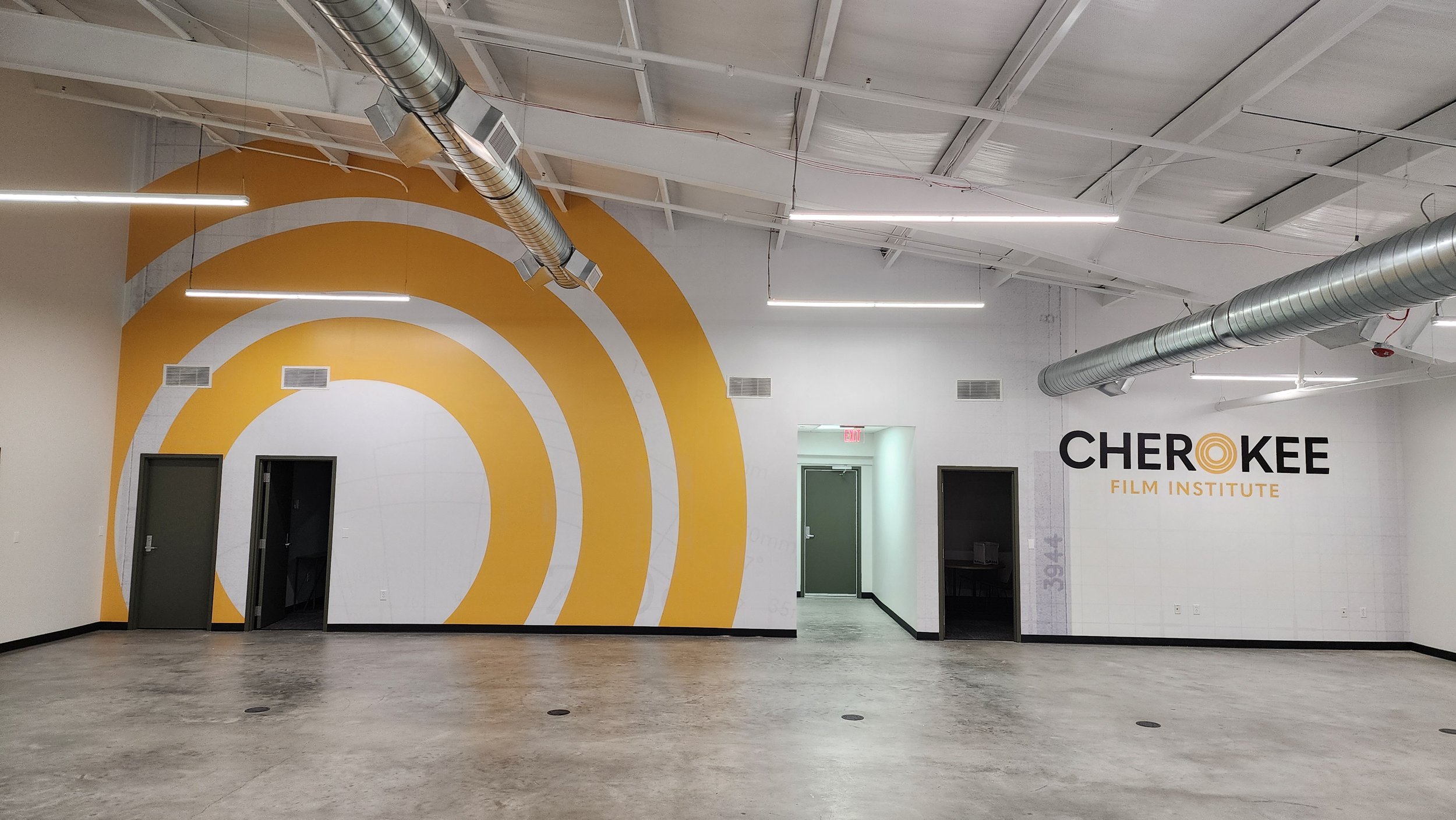 Interior of Cherokee Film Institute showing large white and yellow circular wall design with logo and industrial pipes on the ceiling.