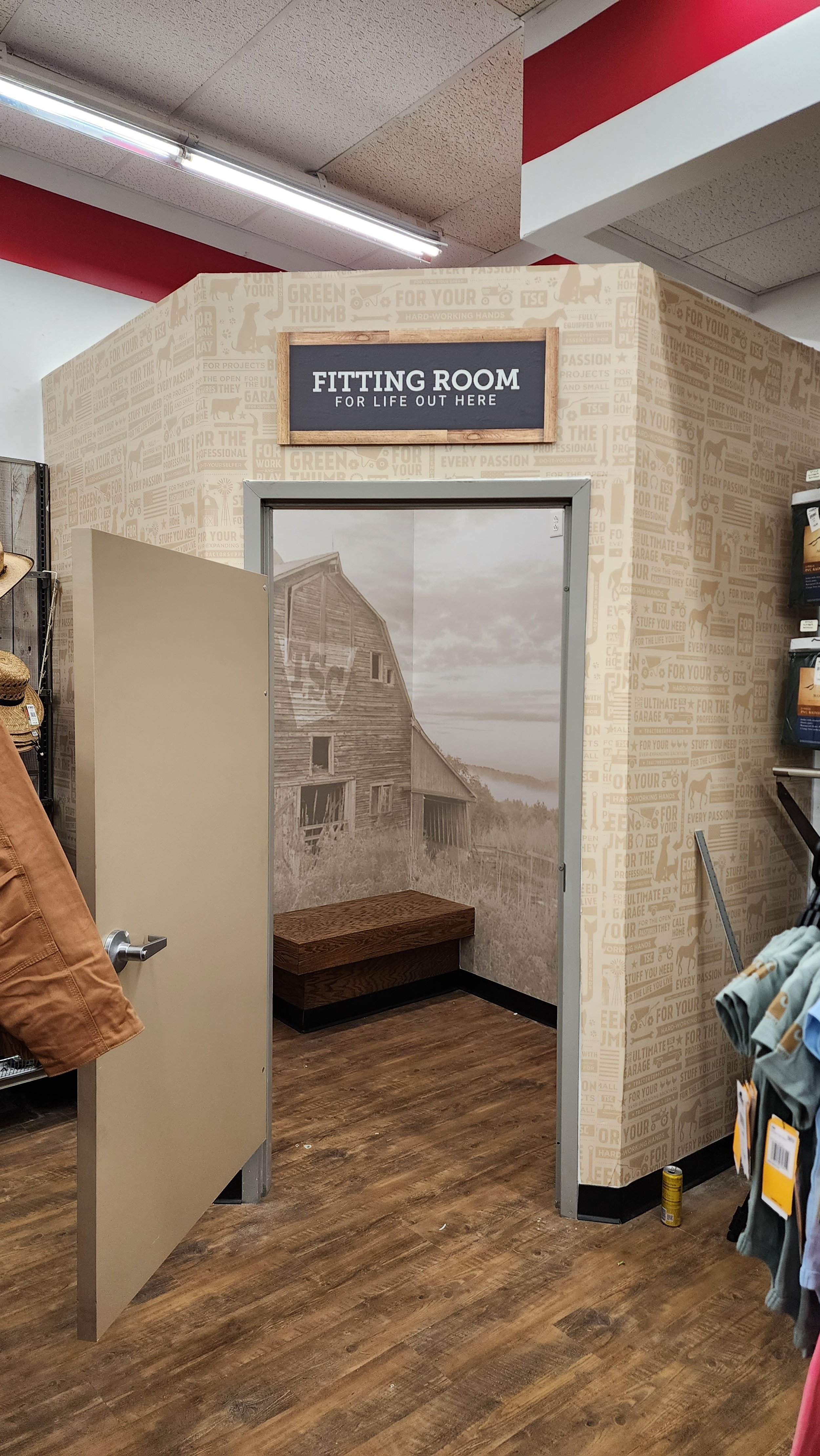 Fitting room entrance in a store, with an open door, wooden bench, and rustic wall mural.