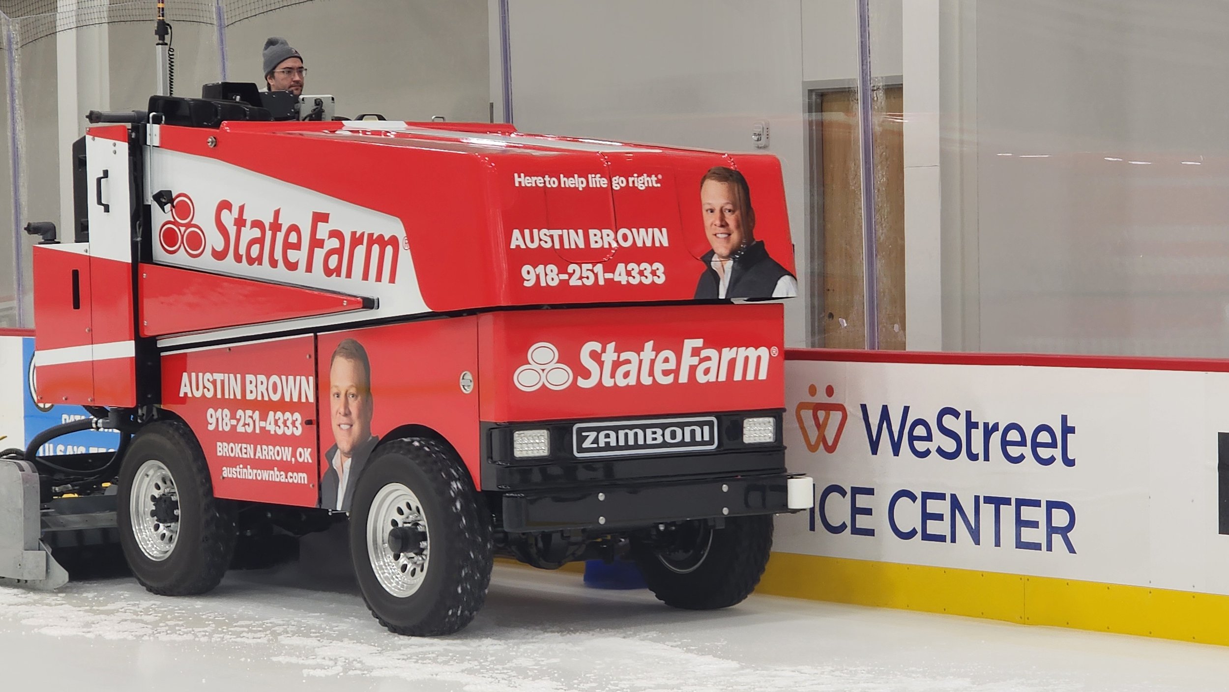 A person operates a red Zamboni with a State Farm advertisement at an ice rink.