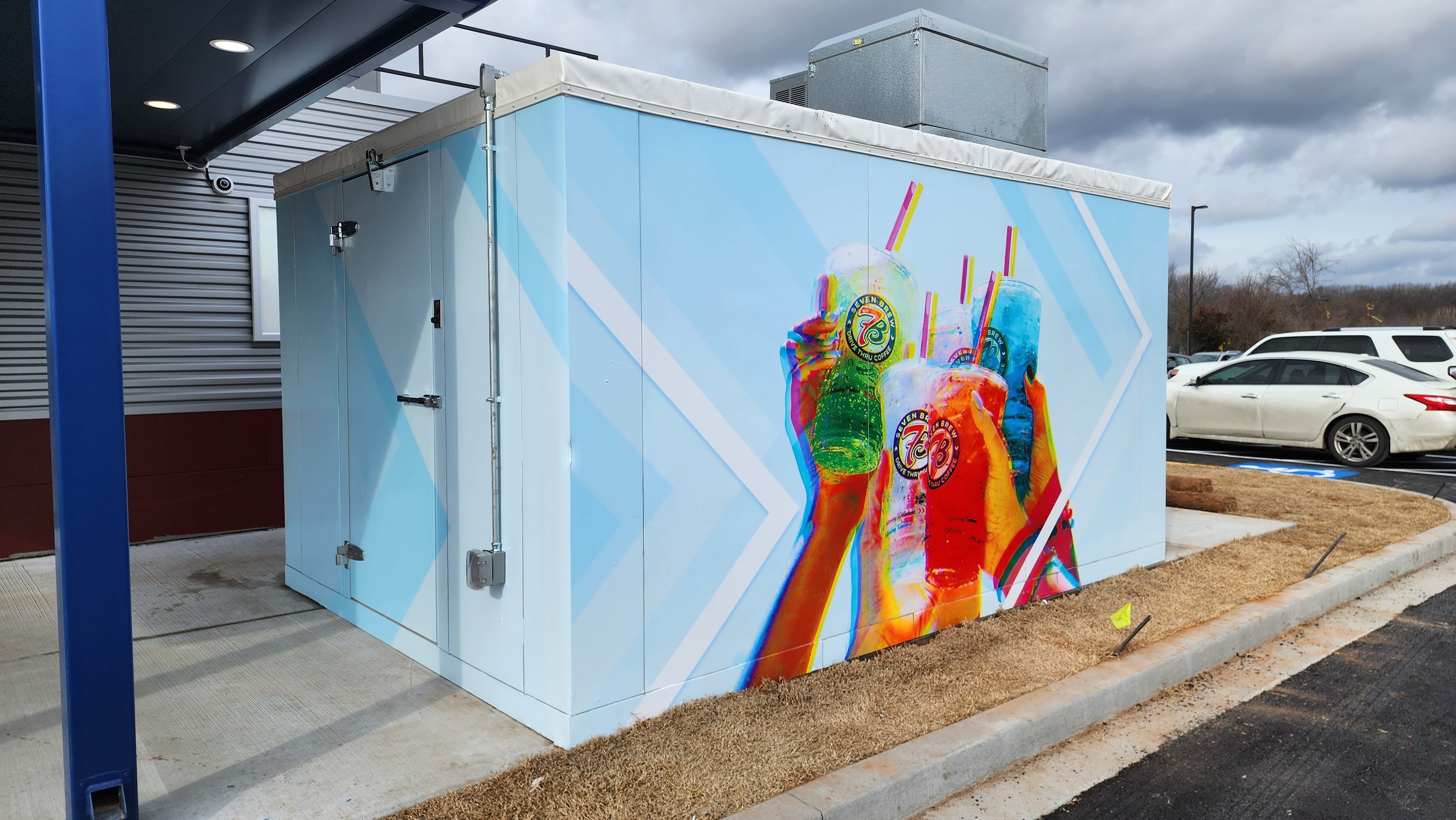 Cooler with colorful drink mural on building exterior.