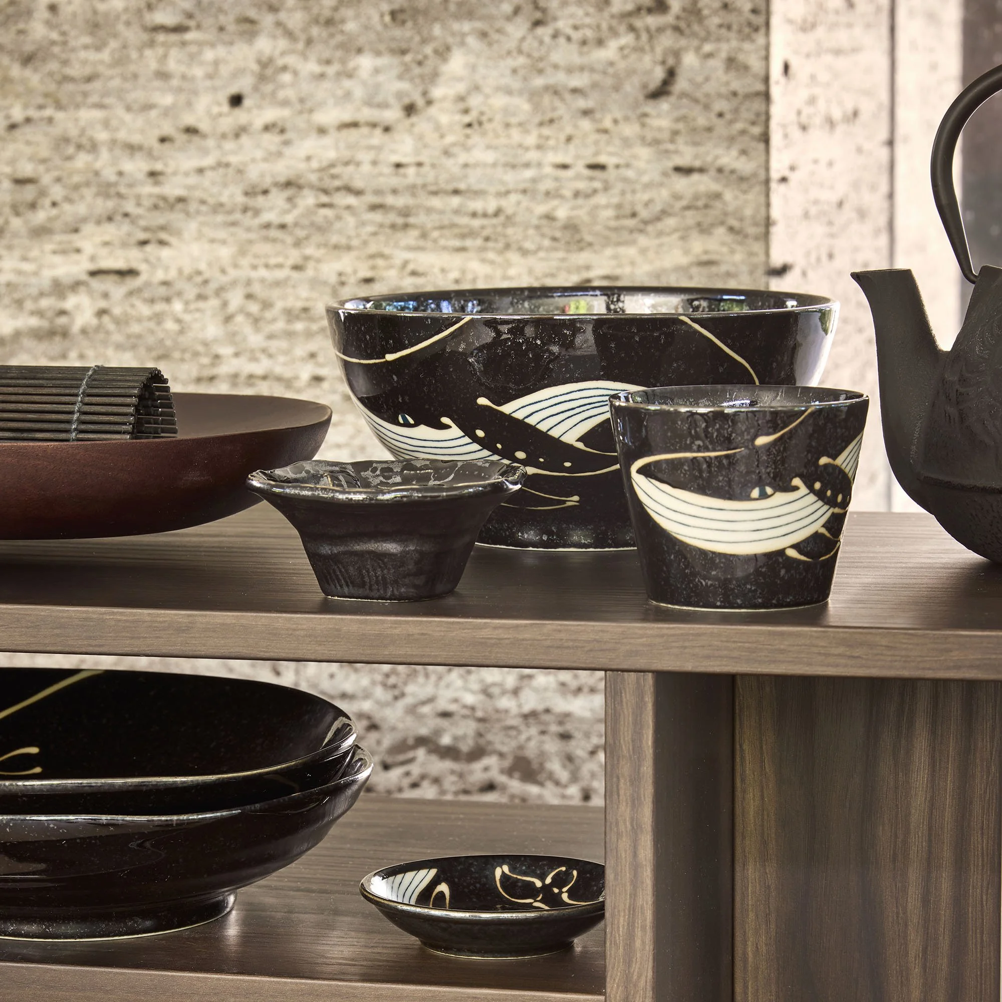 Tokyo Design Studio Black Whale collection — black glazed bowls and cups with whale motif in cream, styled with a cast iron teapot on a wooden console