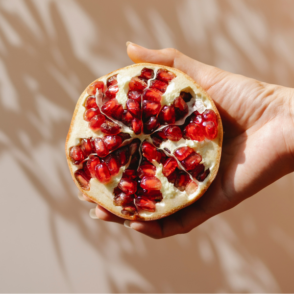 Eine Hand hält eine halbierte Granatapfel mit roten Samen gegen einen neutralen Hintergrund