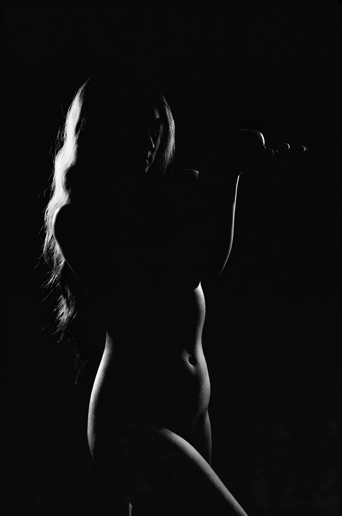 Silhouette d'une femme nue avec une lumière en contre-jour dans un fond noir.