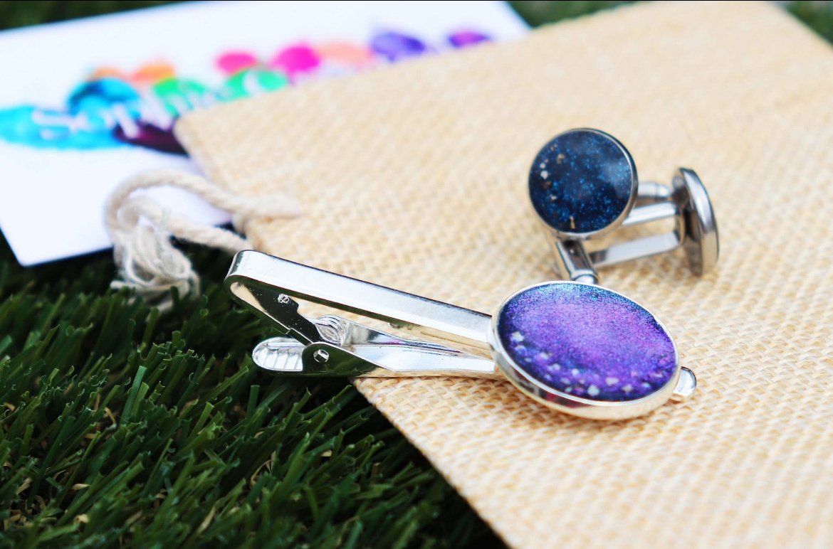 A pair of galaxy-themed cufflinks placed on a beige cloth on grass.