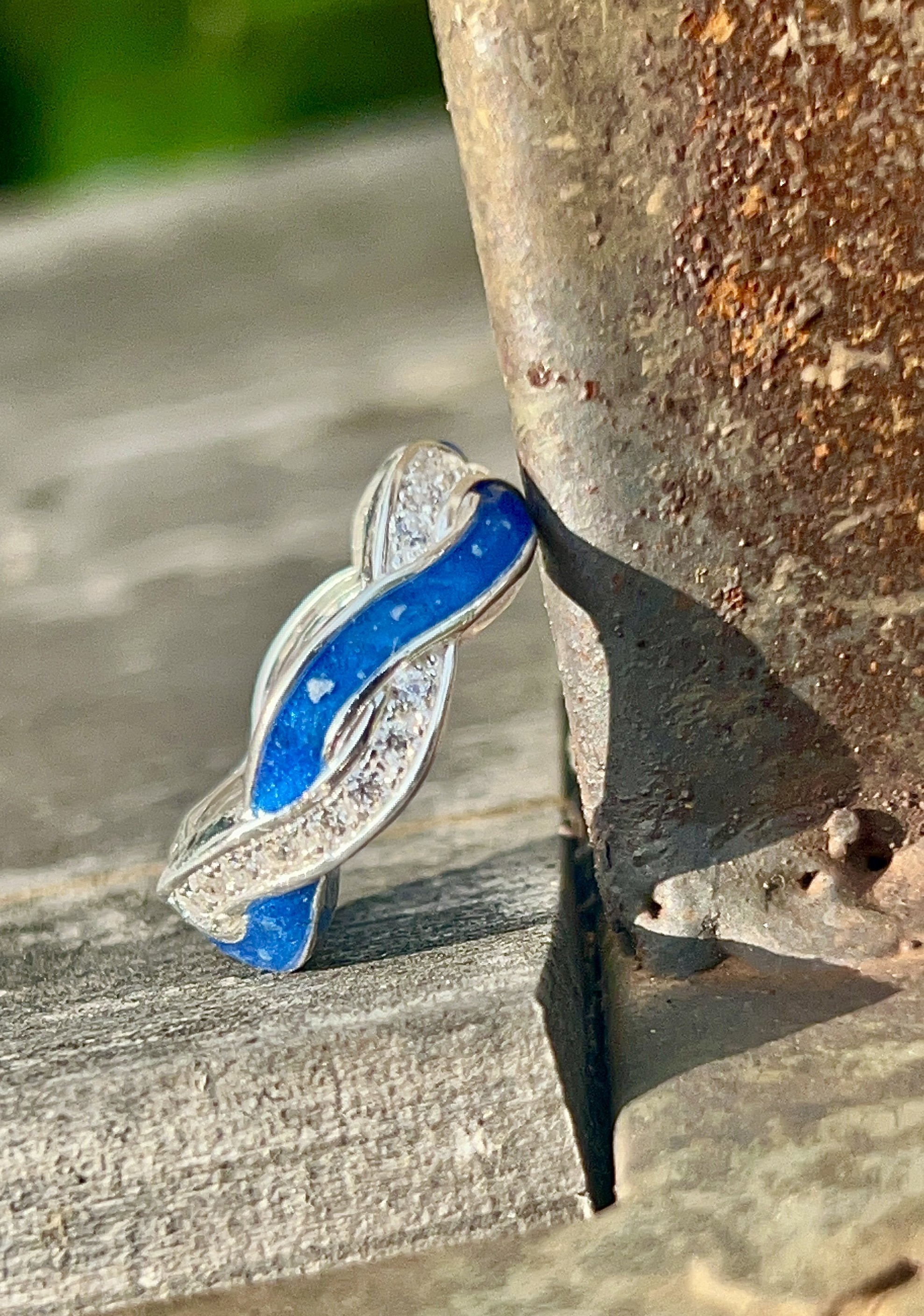 Close-up of a silver ring with a blue stone and small clear stones, placed on a wooden surface next to a rusty metal object.
