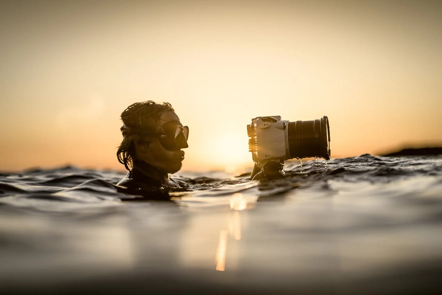 George Karbus swimming in water during sunset, holding a camera.