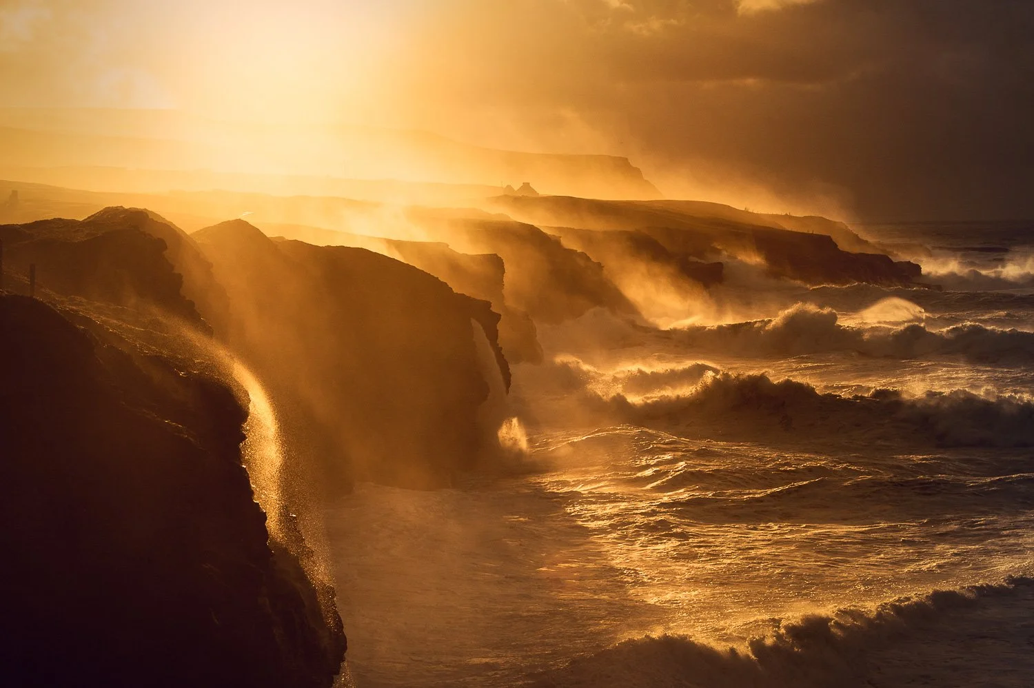 Sunset over rugged Doolin cliffs with ocean waves crashing, illuminated in warm golden light.
