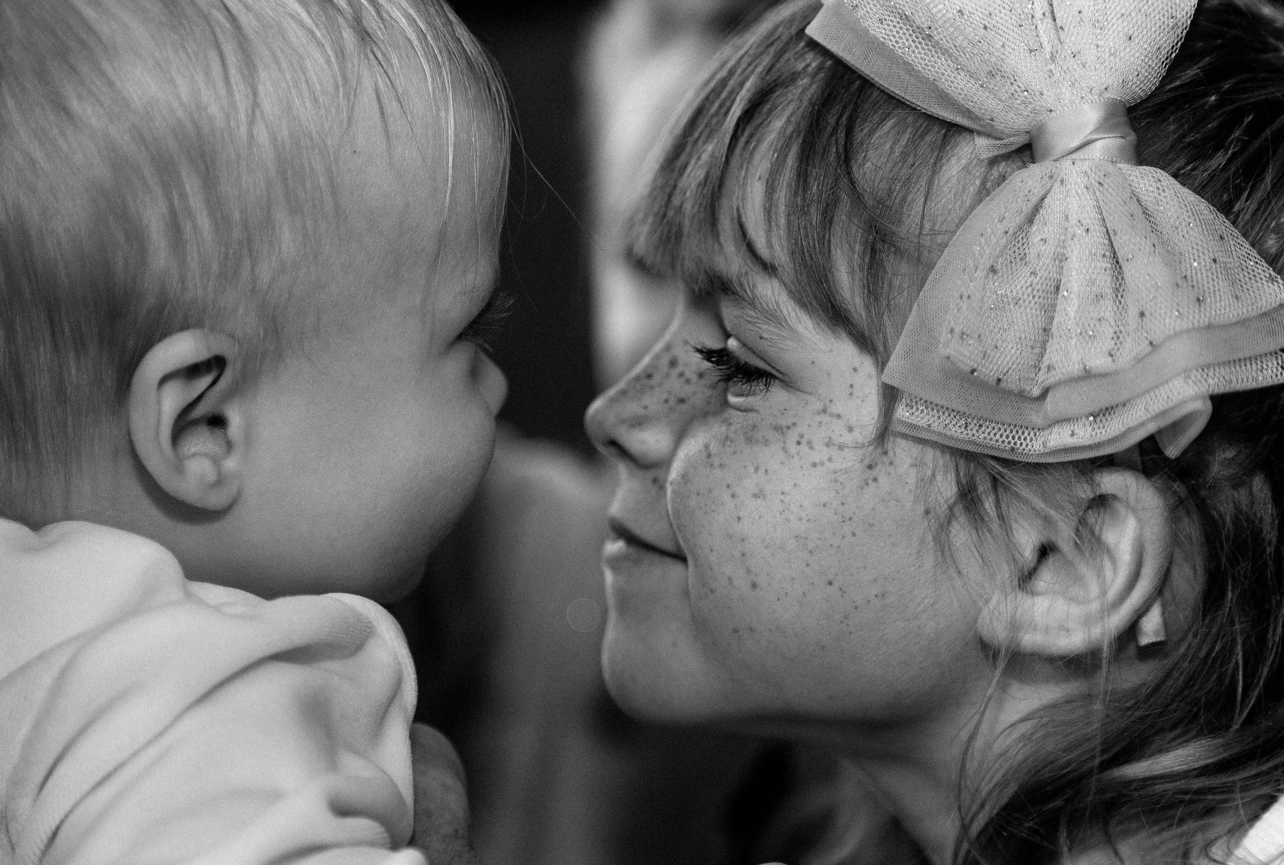 Black and white image of a baby girl and a little girl looking at each other 
