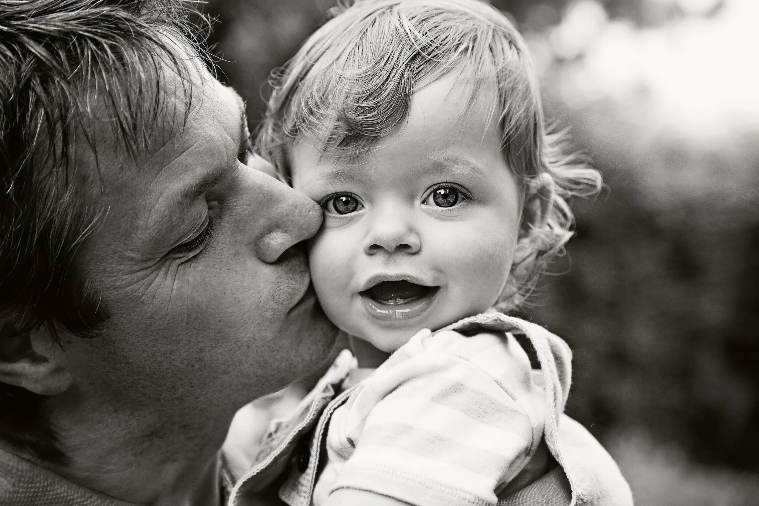 Black and white image of a father kissing his young son on the cheek 
