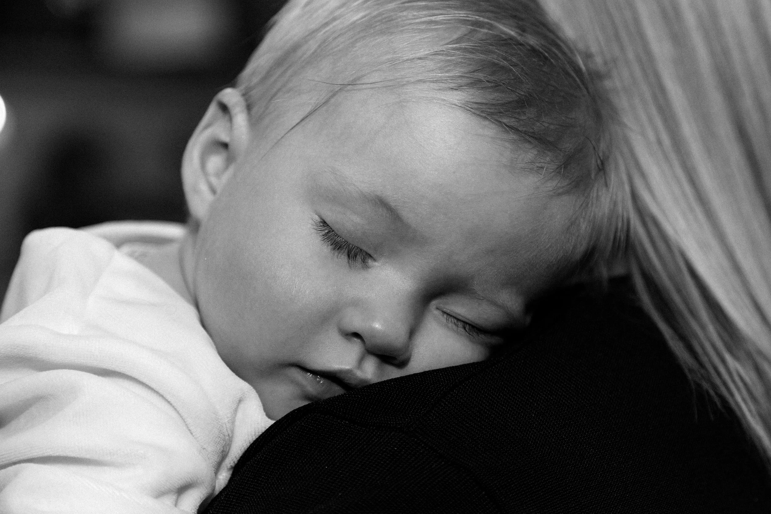 Black and white image of a baby fast asleep on her mums shoulders 