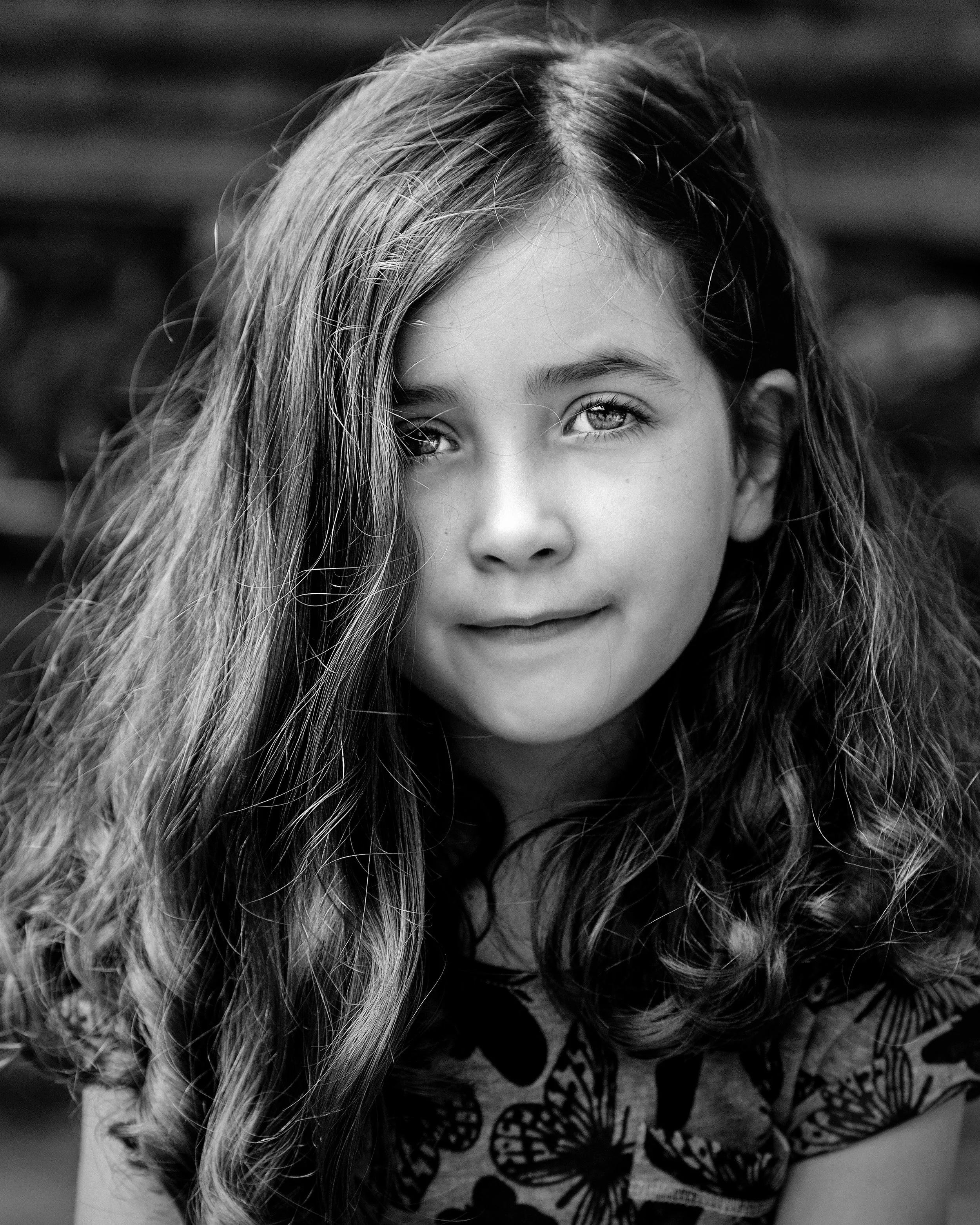 A black and white portrait of a young girl with wavy hair, smiling softly, looking directly at the camera.
