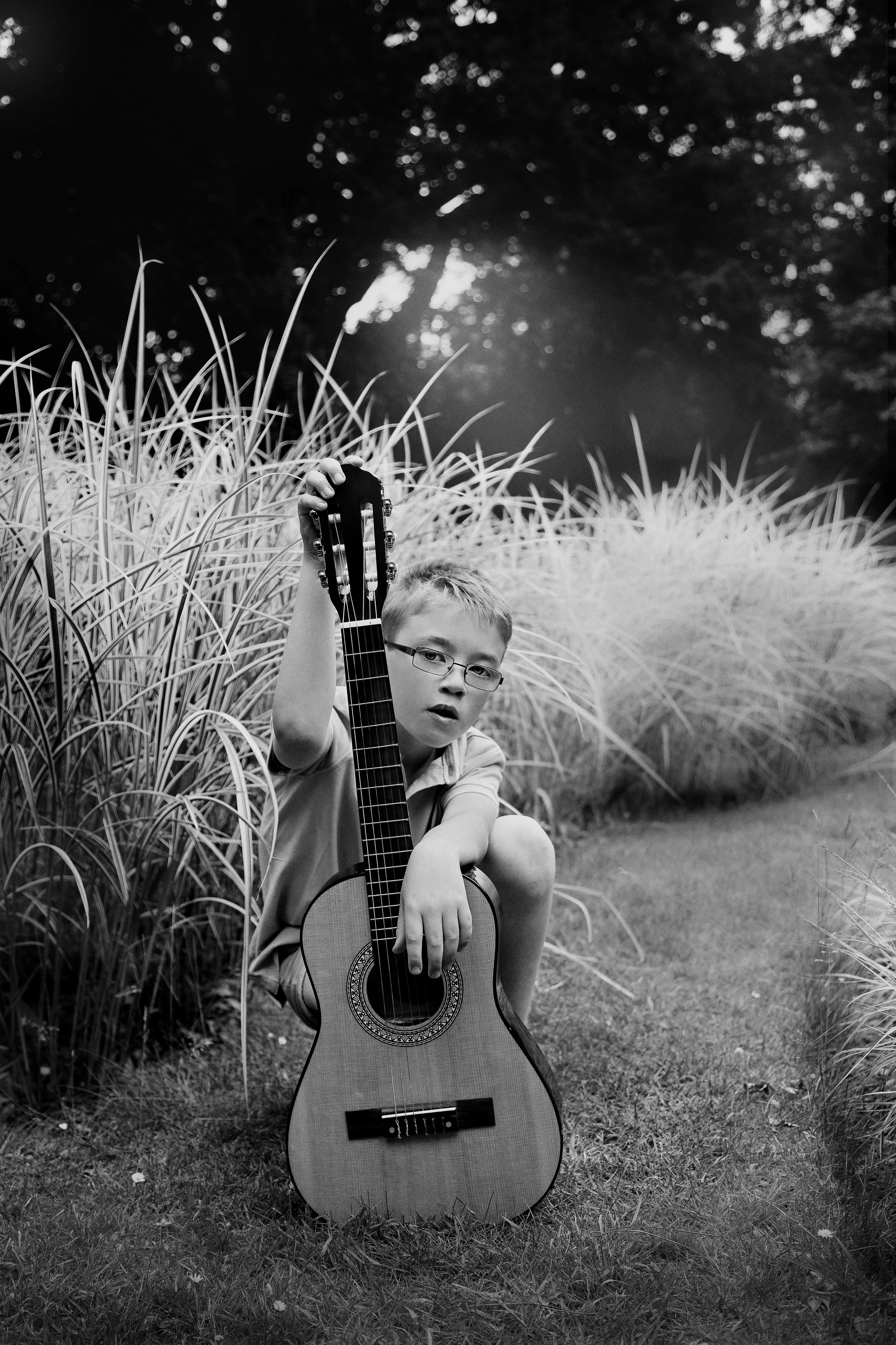 Black and white image of a young boy with his guitar in a garden