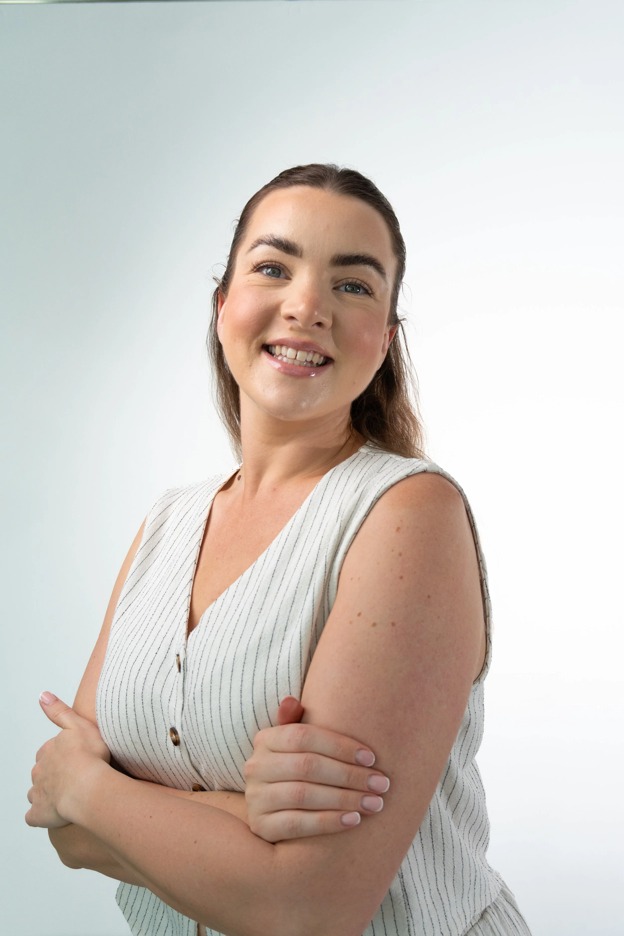 Portrait of a smiling woman with crossed arms, wearing a sleeveless striped top, against a plain white background.