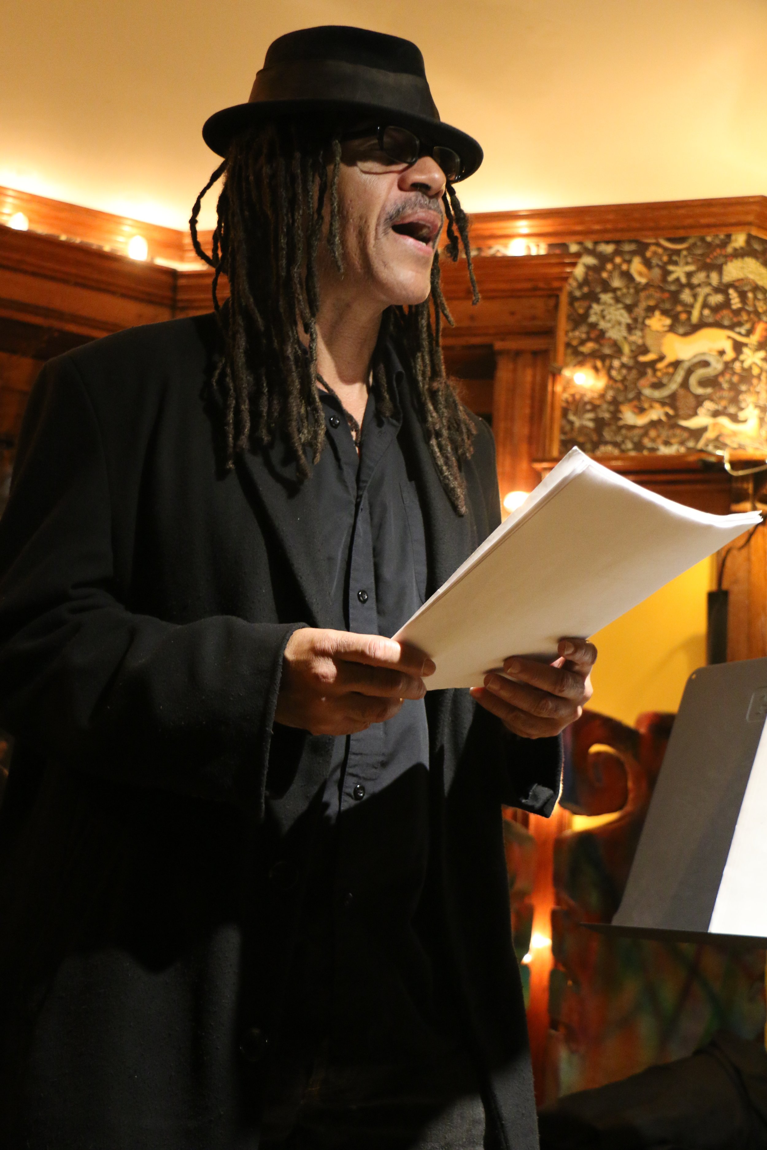 Person with dreadlocks and a hat reading from a script