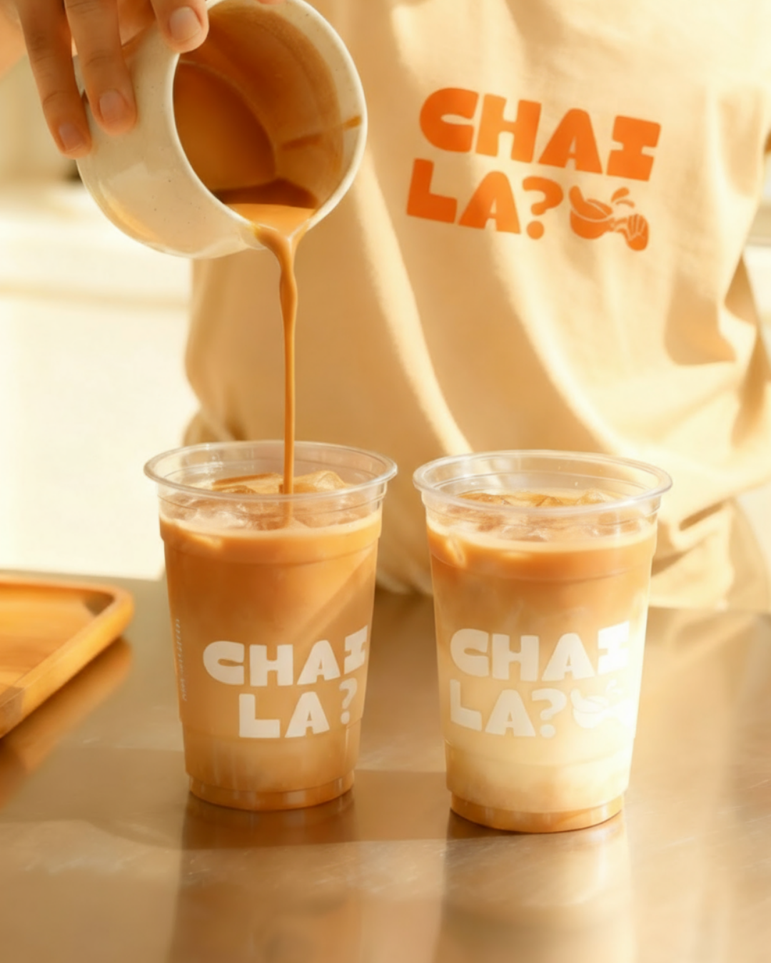 Pouring iced chai latte into branded plastic cups