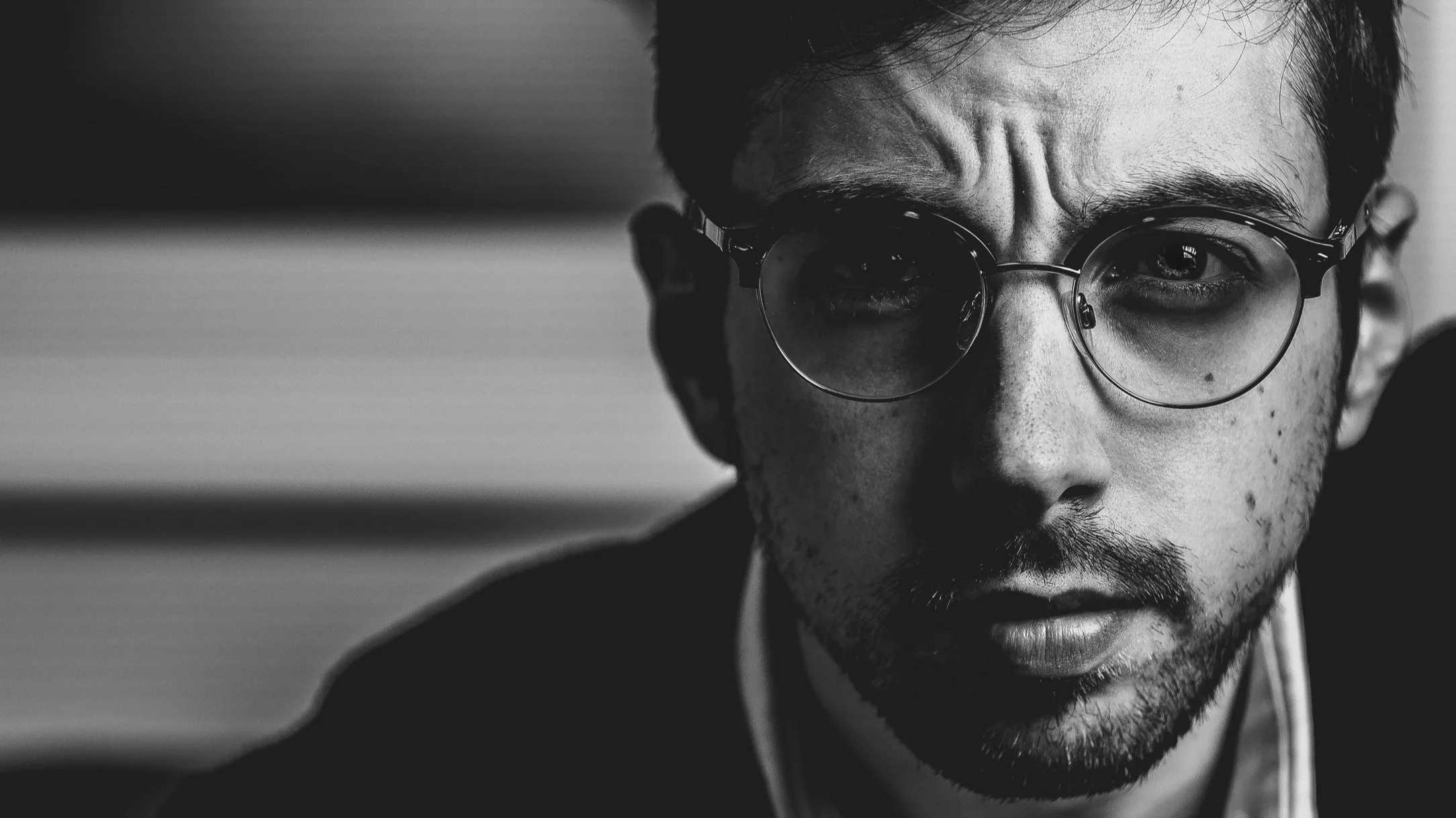 Close-up black and white portrait of a man with glasses looking directly at the camera.